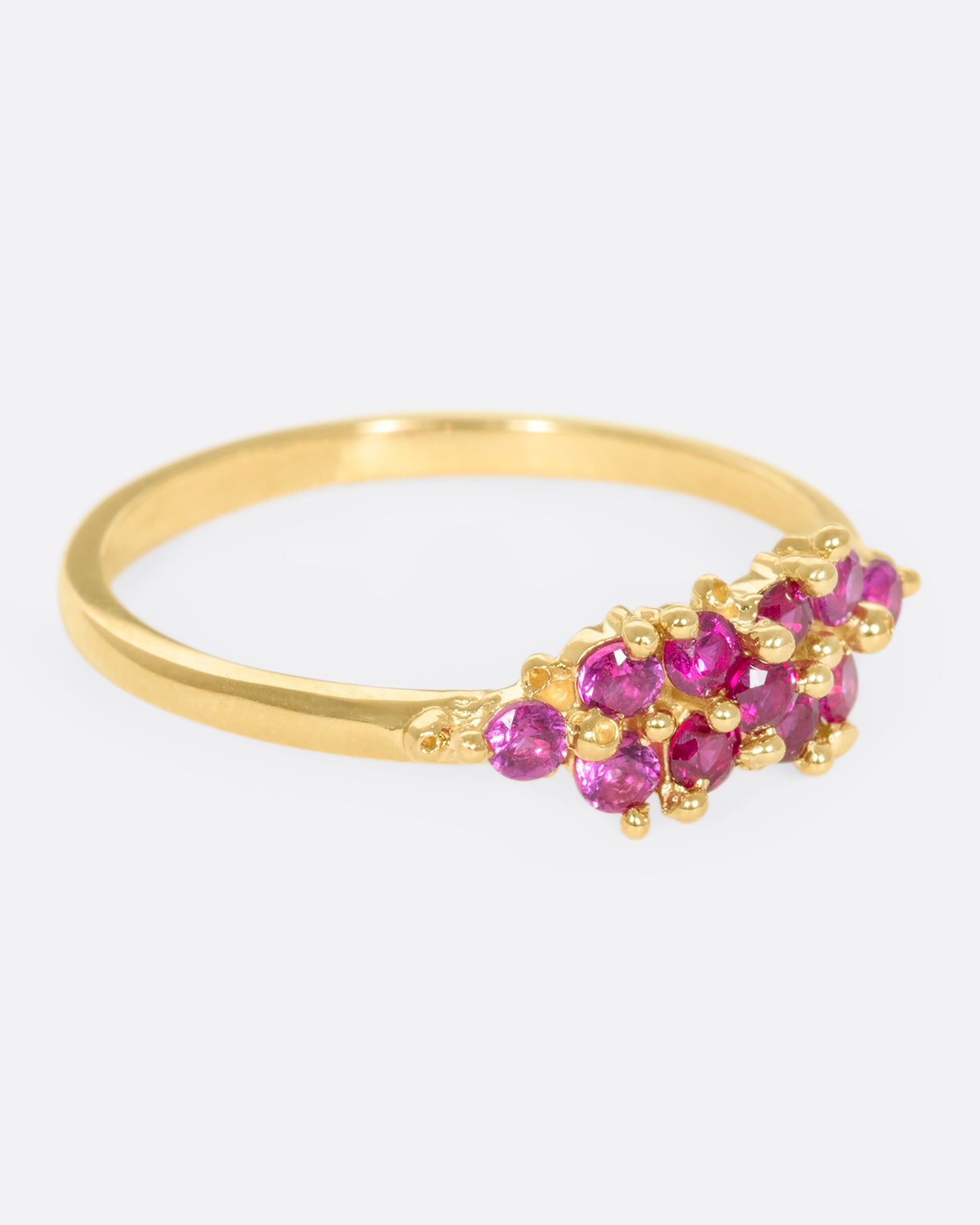 A yellow gold ring with a cluster of rubies arranged on the face. Shown from the side.