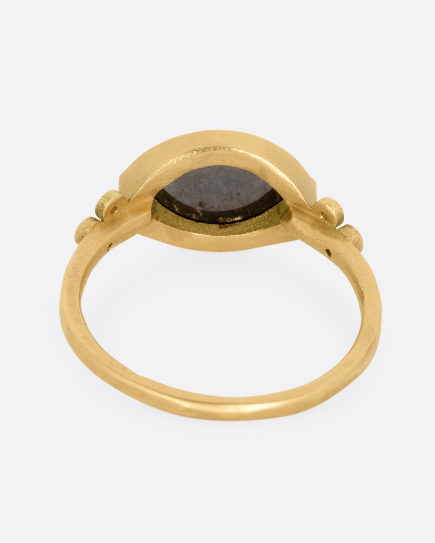 A yellow gold ring with a wide eye-shaped black marquise diamond flanked by a trio of white diamonds, shown from the back.