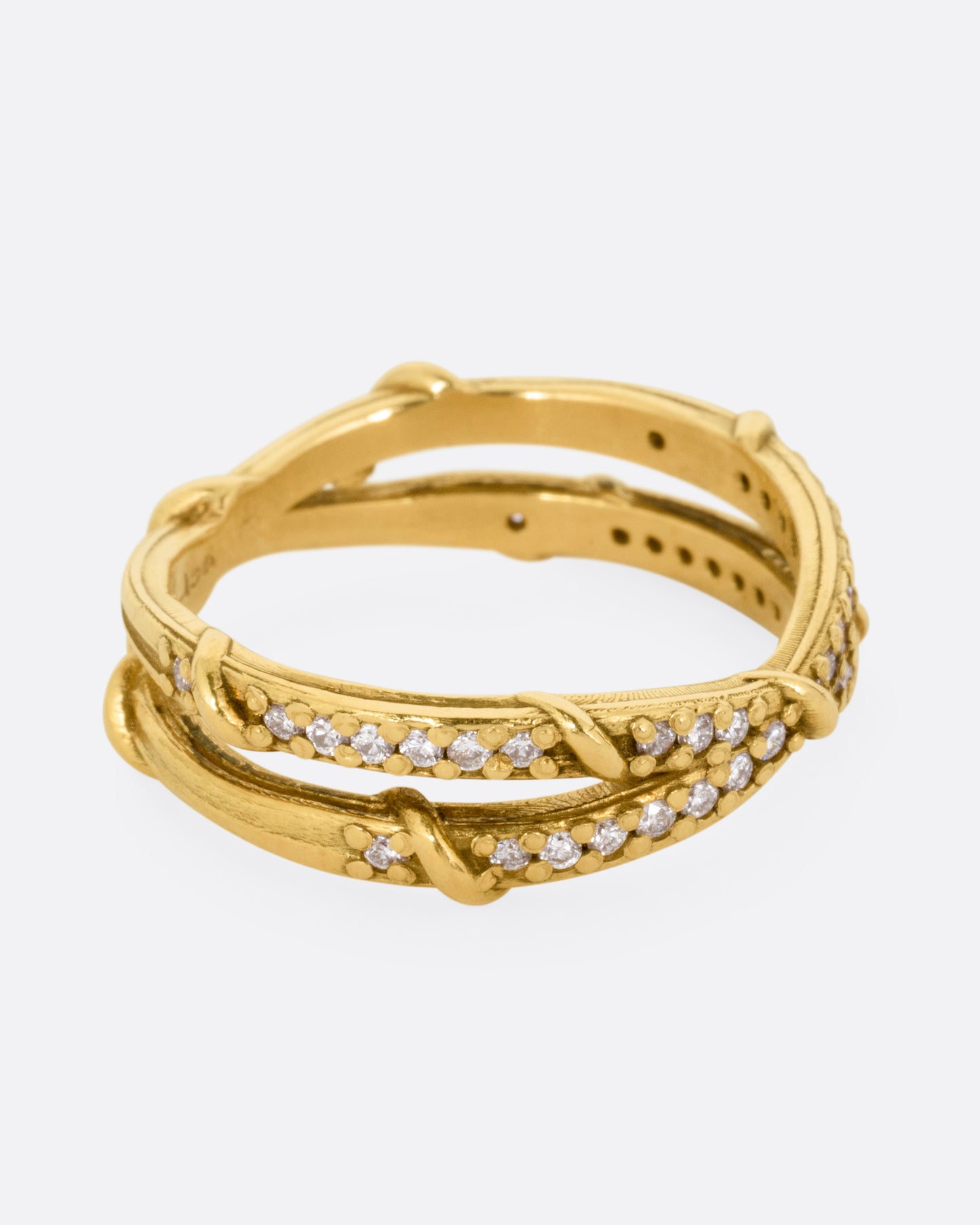 A yellow gold ring with two eternity bands intersecting at the middle and wrapped in vines and colorless diamonds. Shown from the side.