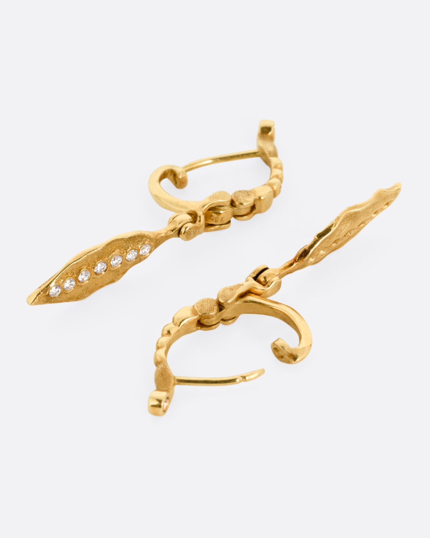 A pair of gold drop earrings with dangling leaves and diamond accents, shown from the side with one earring open.