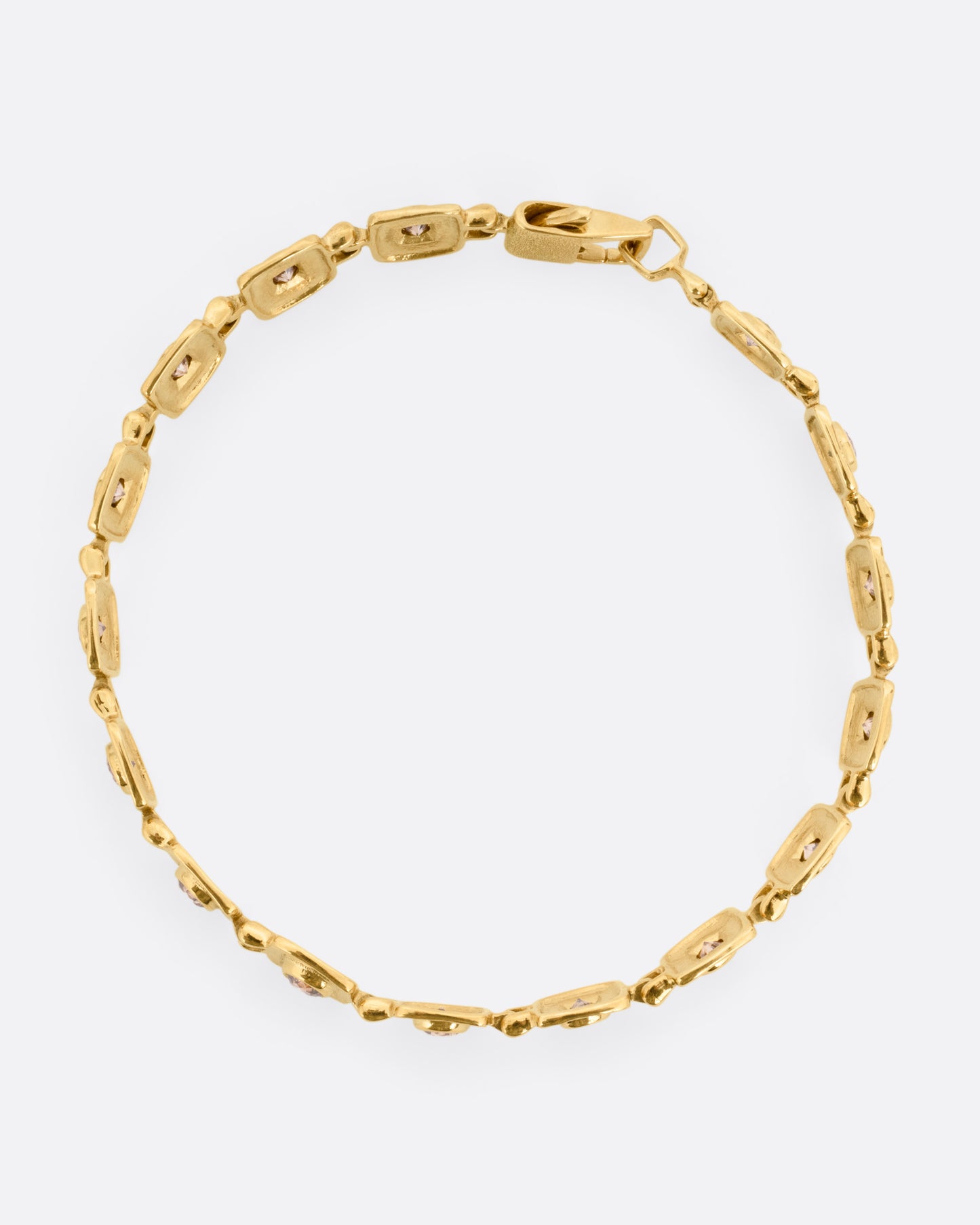 A yellow gold bracelet with squared stations, each with a brown diamond. Shown from the top.