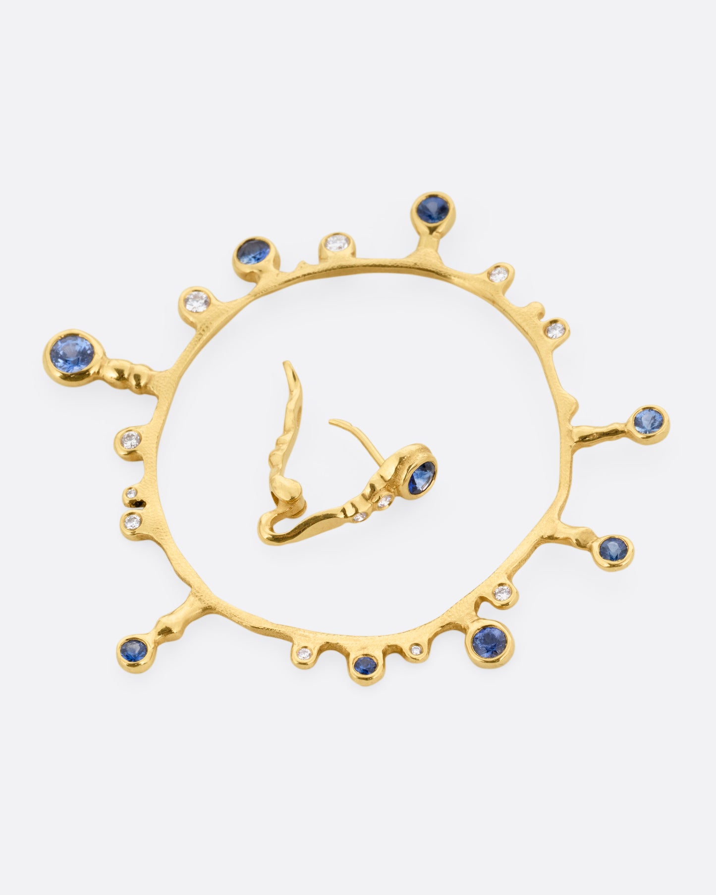 A yellow gold hoop sunburst earring with diamonds and sapphires. Shown open lying on its side.