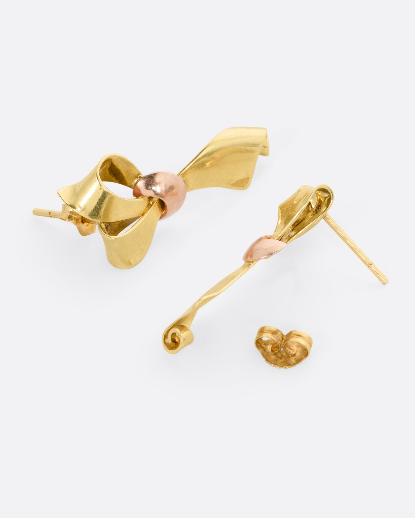 A pair of yellow gold ribbon shaped earrings with a rose gold knot, shown from the side with one earring open.