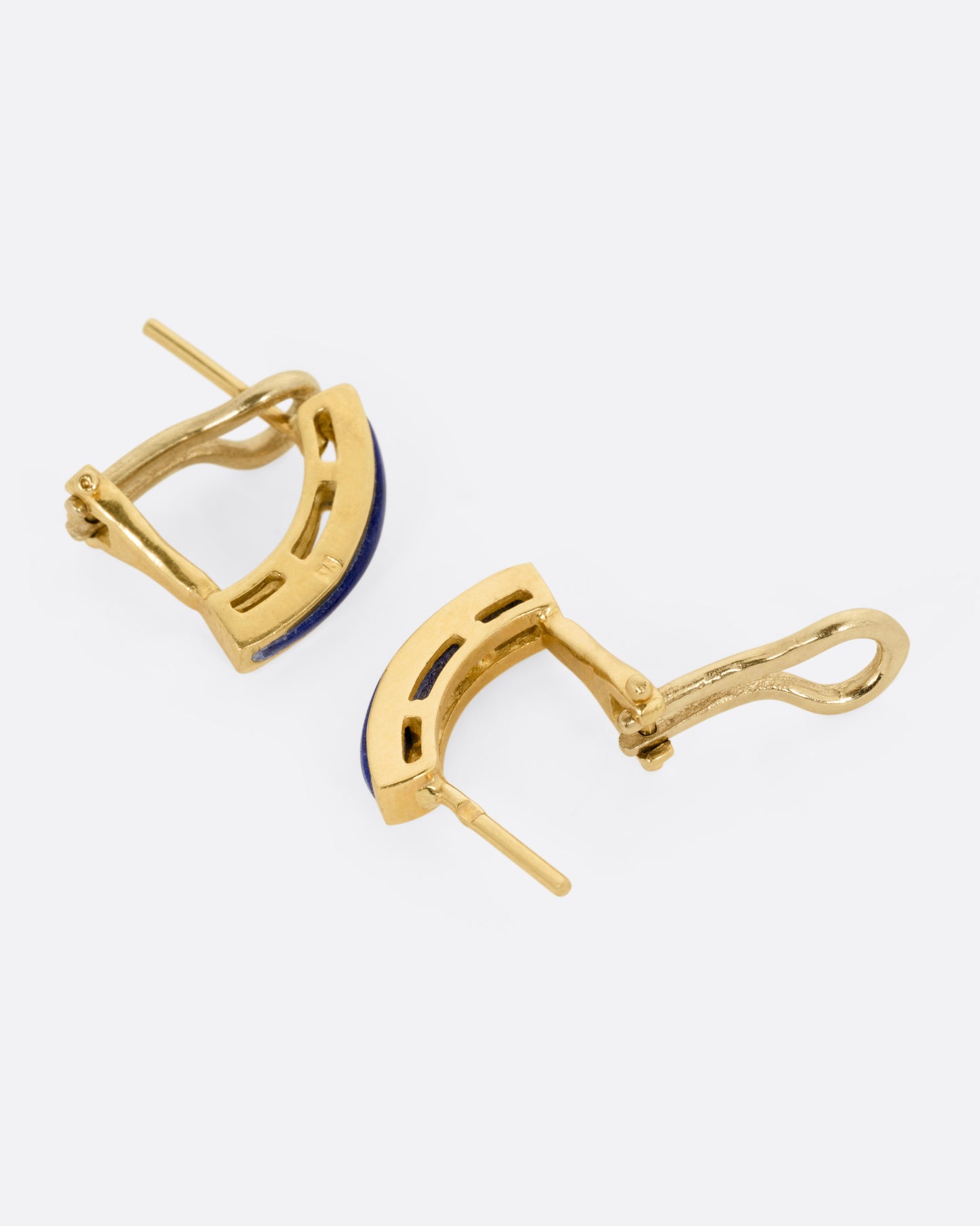 A pair of yellow gold earrings with arched lapis bars, shown lying on their sides with one earring open.