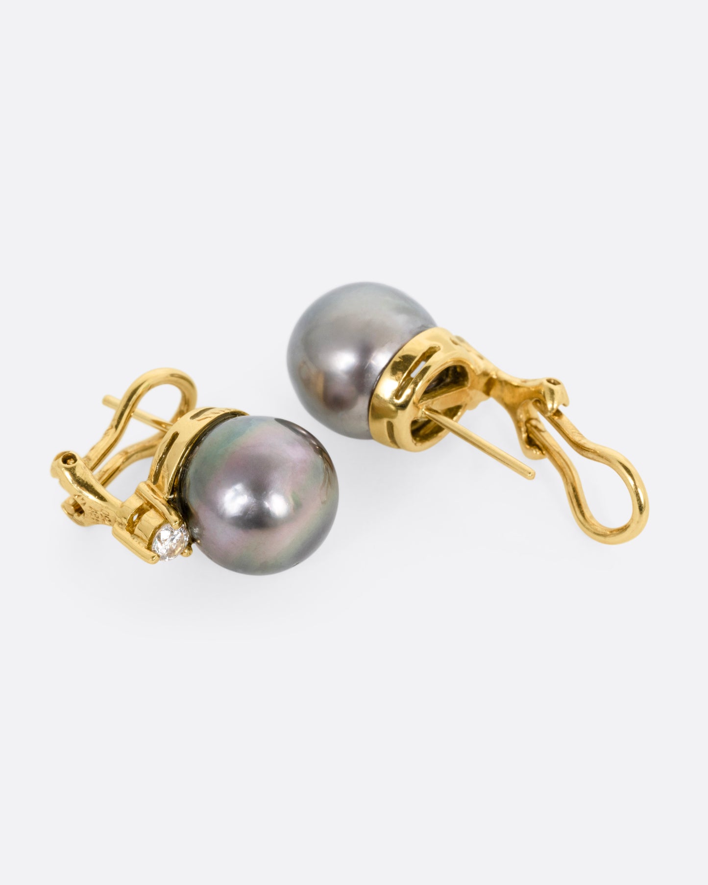 A yellow gold earring with a black pearl, and a white diamond, shown lying on their sides, with one earring open.