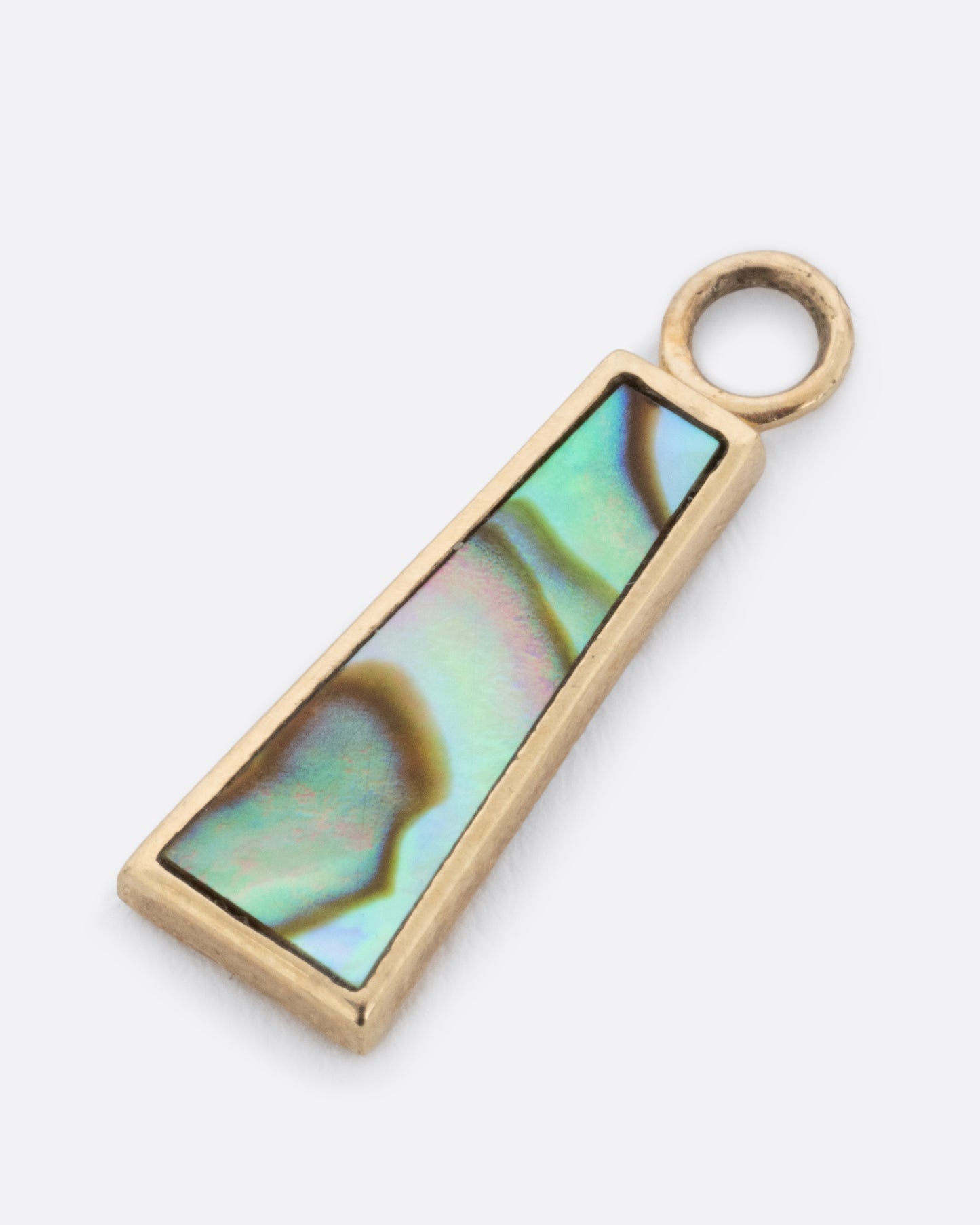 A yellow gold trapezoid dangle with abalone inlay. Shown lying flat diagonally from the front.