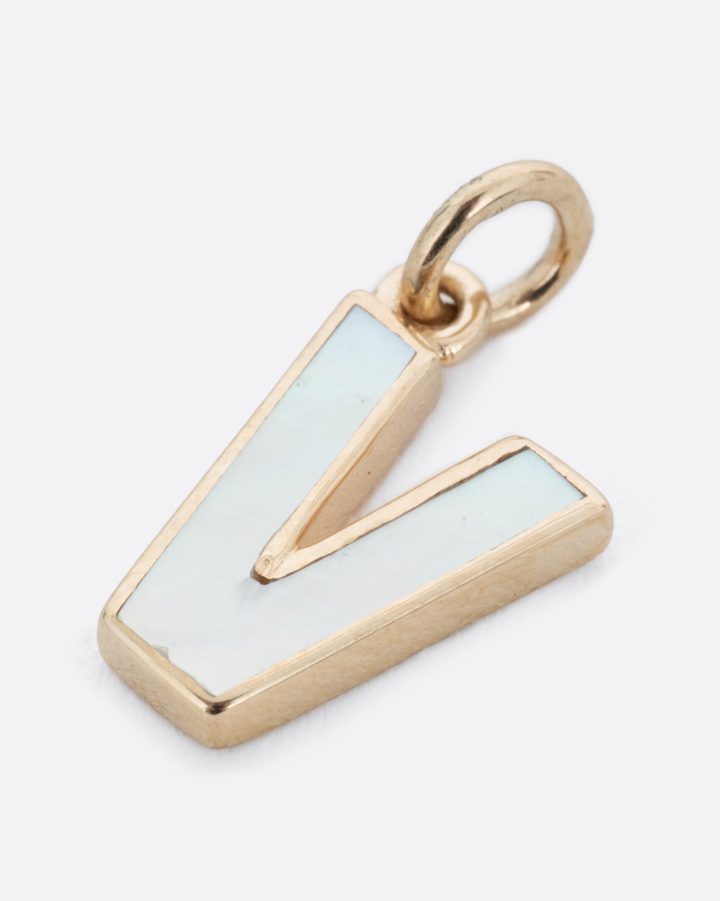 A mother of pearl V charm set in yellow gold with a yellow gold jump ring and hoop. Shown lying flat at a diagonal from the front.