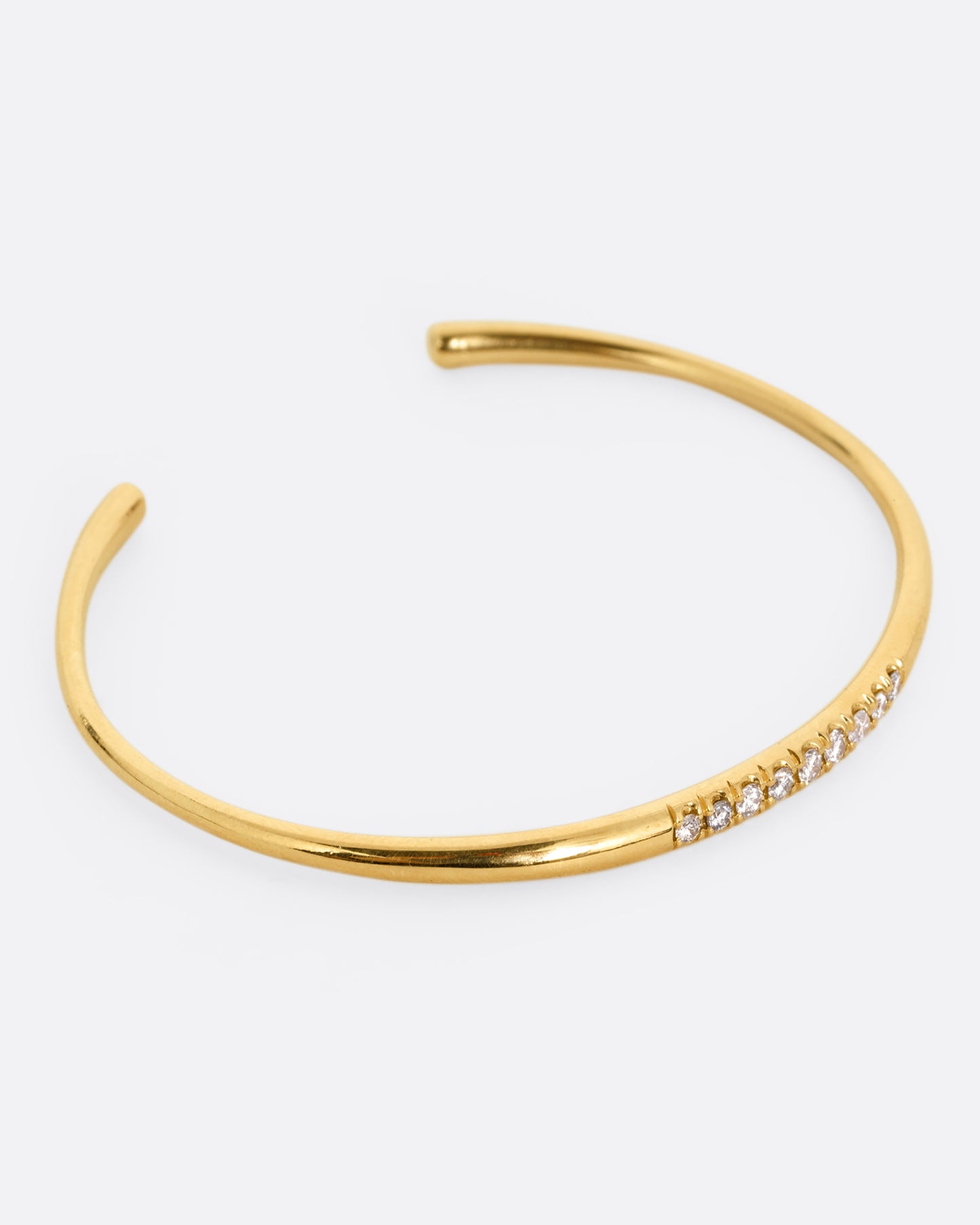 A narrow yellow gold cuff bracelet with a queue of diamonds at the center. Shown from the side.