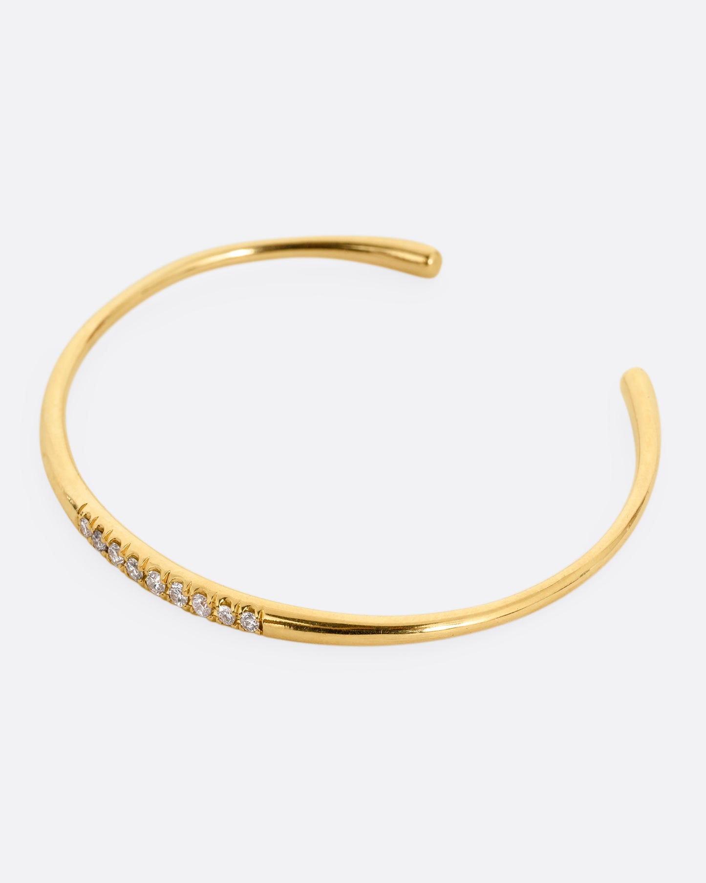 A narrow yellow gold cuff bracelet with a queue of diamonds at the center. Shown from the side.