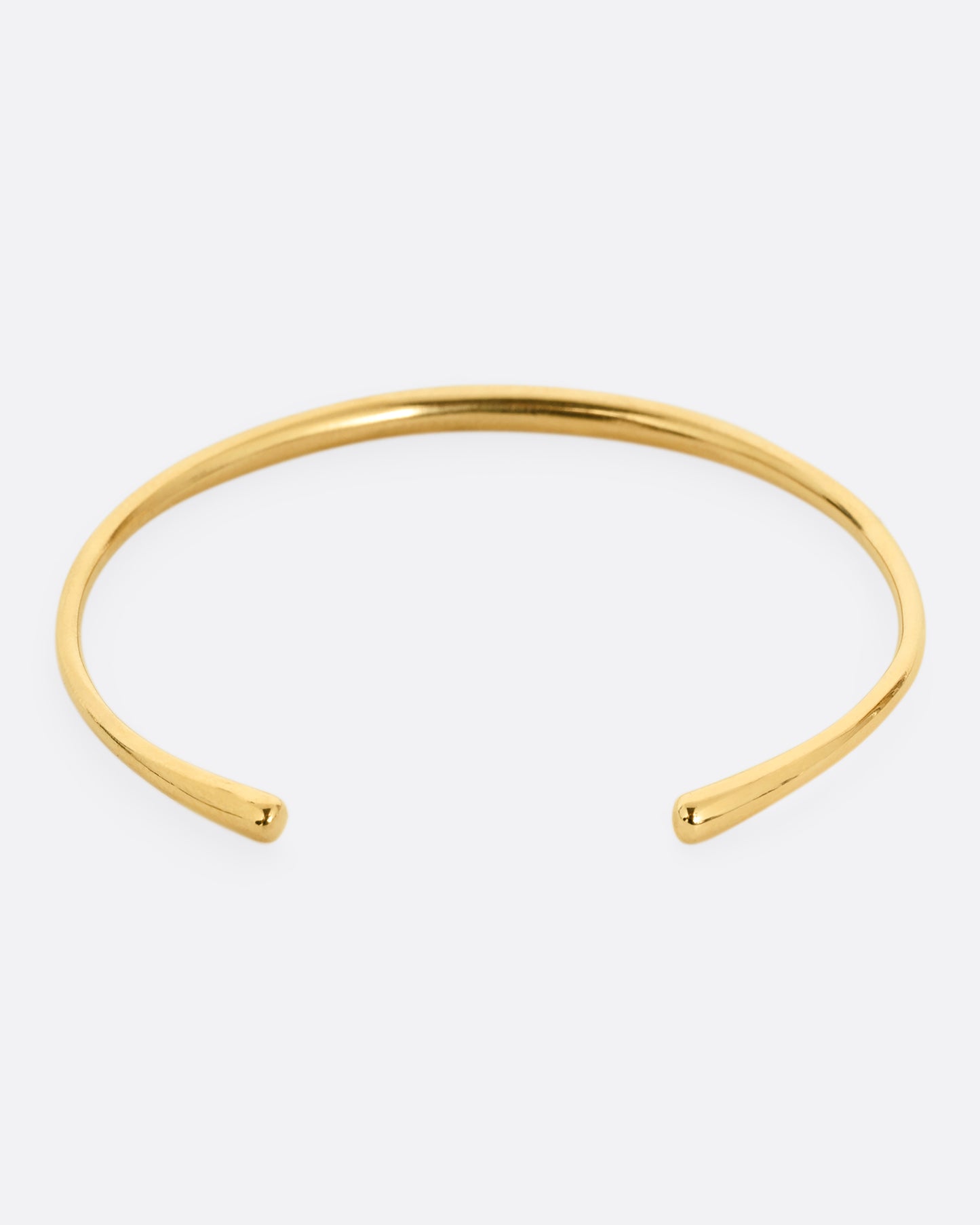 A narrow yellow gold cuff bracelet with a queue of diamonds at the center. Shown from the back.