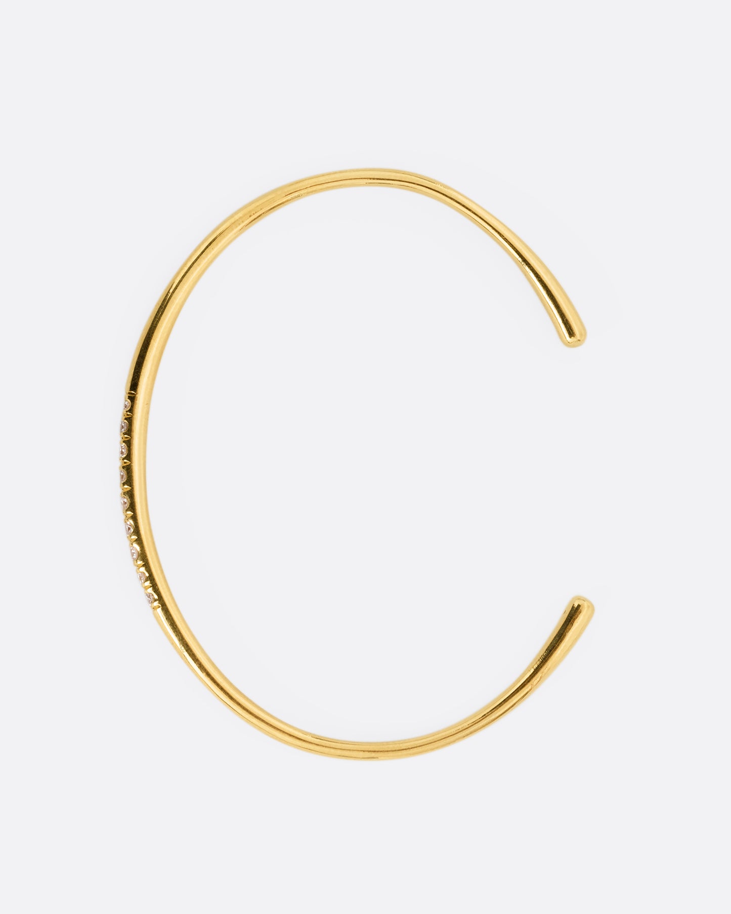 A narrow yellow gold cuff bracelet with a queue of diamonds at the center. Shown standing up from the side.