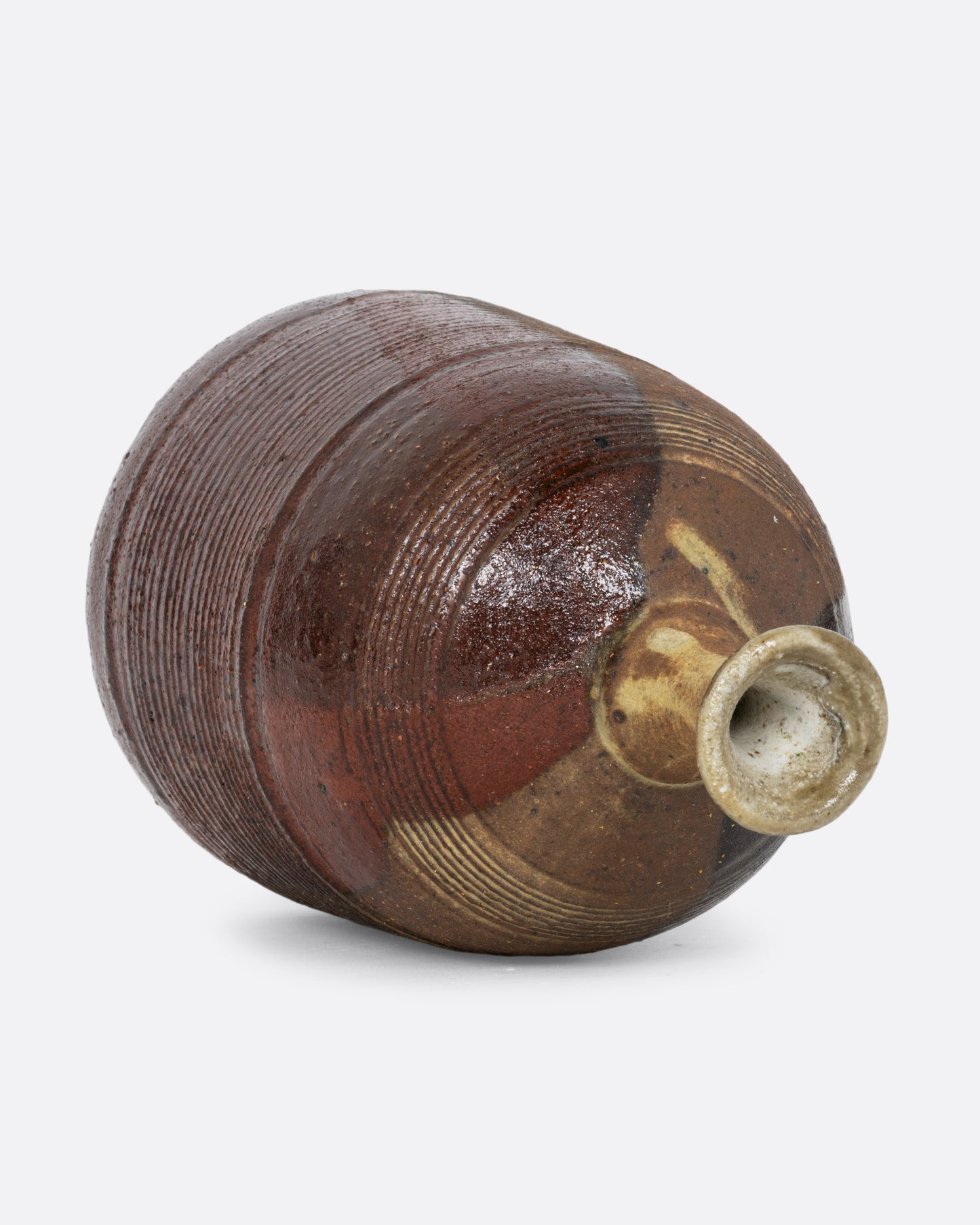 A vase with a brown split contrast glaze and ribbed texture. Shown diagonally on its side from the top.