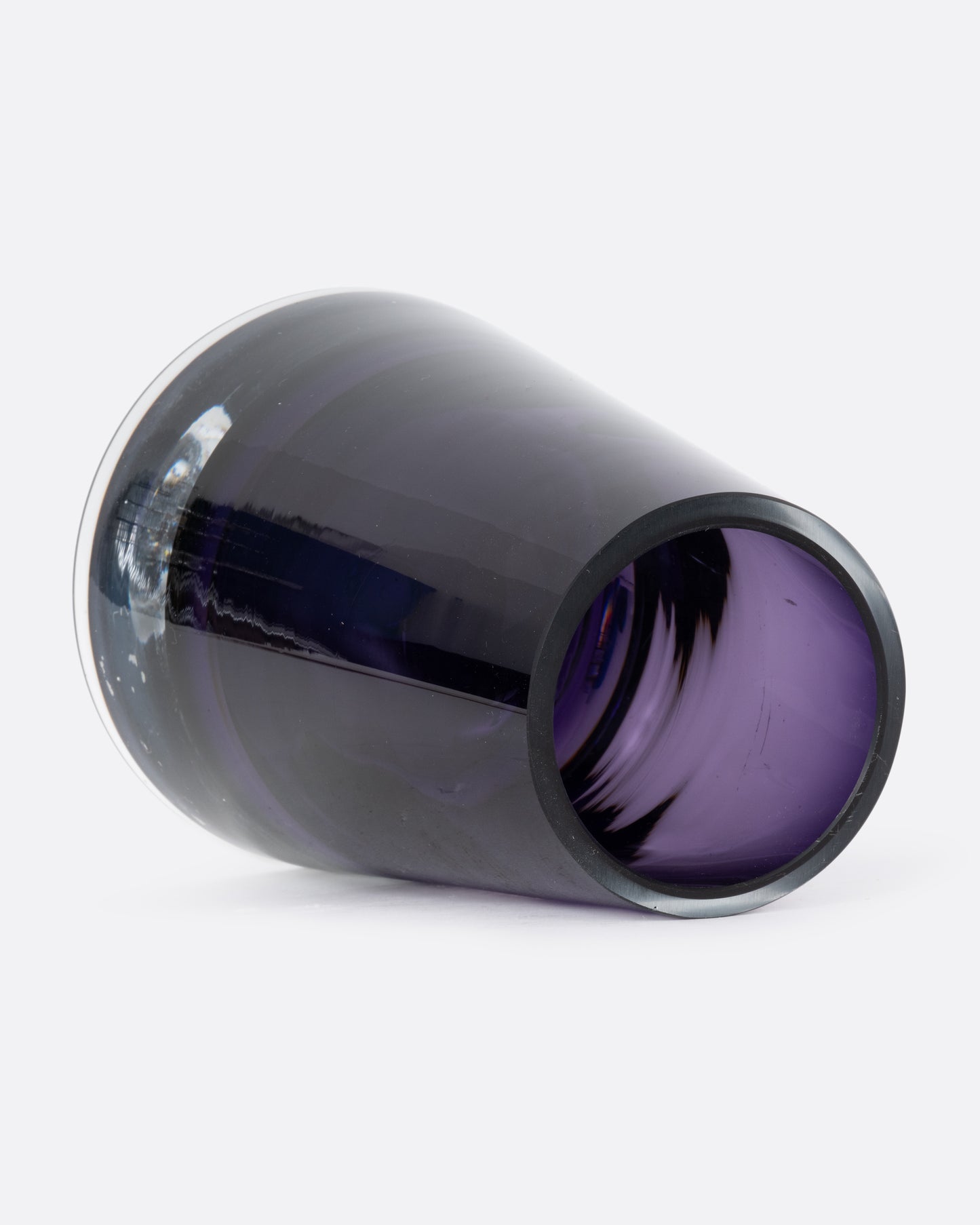 An aubergine glass vase with a wide base and more narrow top. Shown lying on its side from the top.