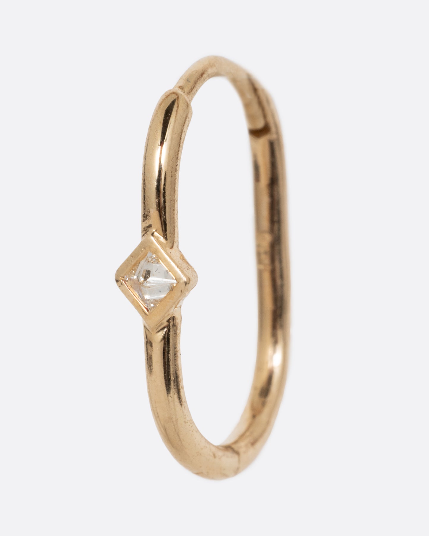 A single yellow gold clicker hoop with a reverse set diamond at the center. Shown from the side.