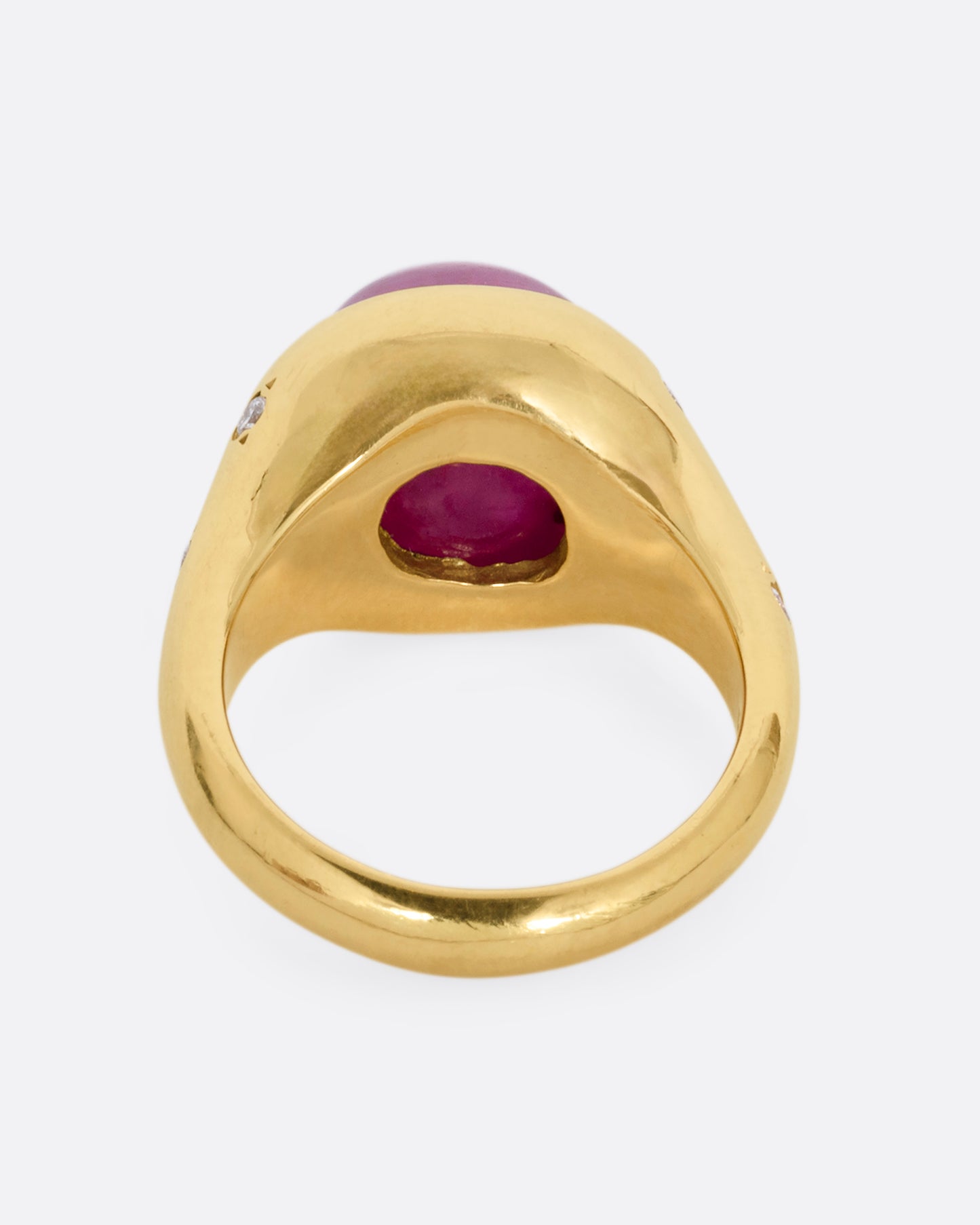 A yellow gold signet ring with a ruby cabochon and diamonds on either shoulder. Shown from the back.