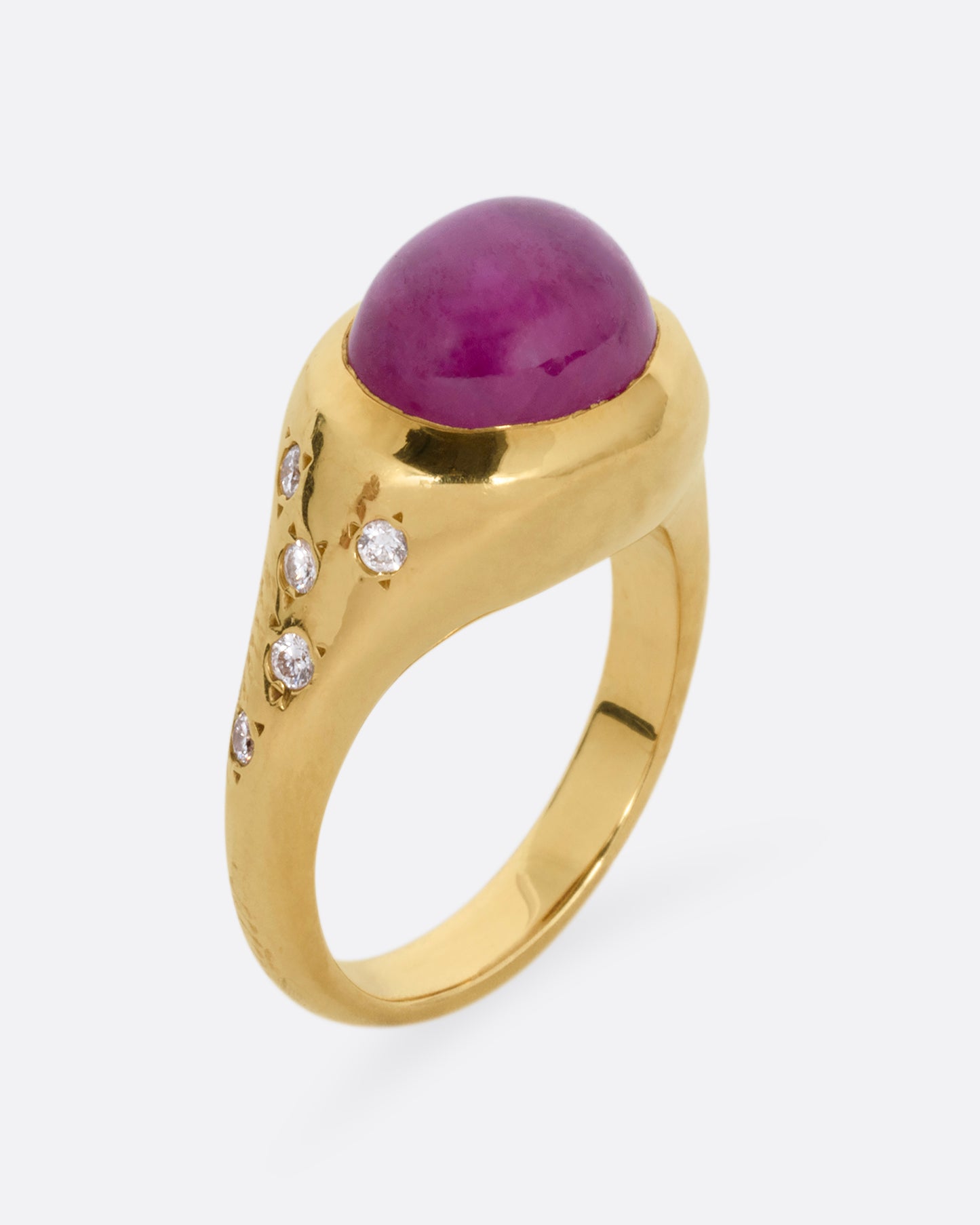 A yellow gold signet ring with a ruby cabochon and diamonds on either shoulder. Shown from the side standing up.