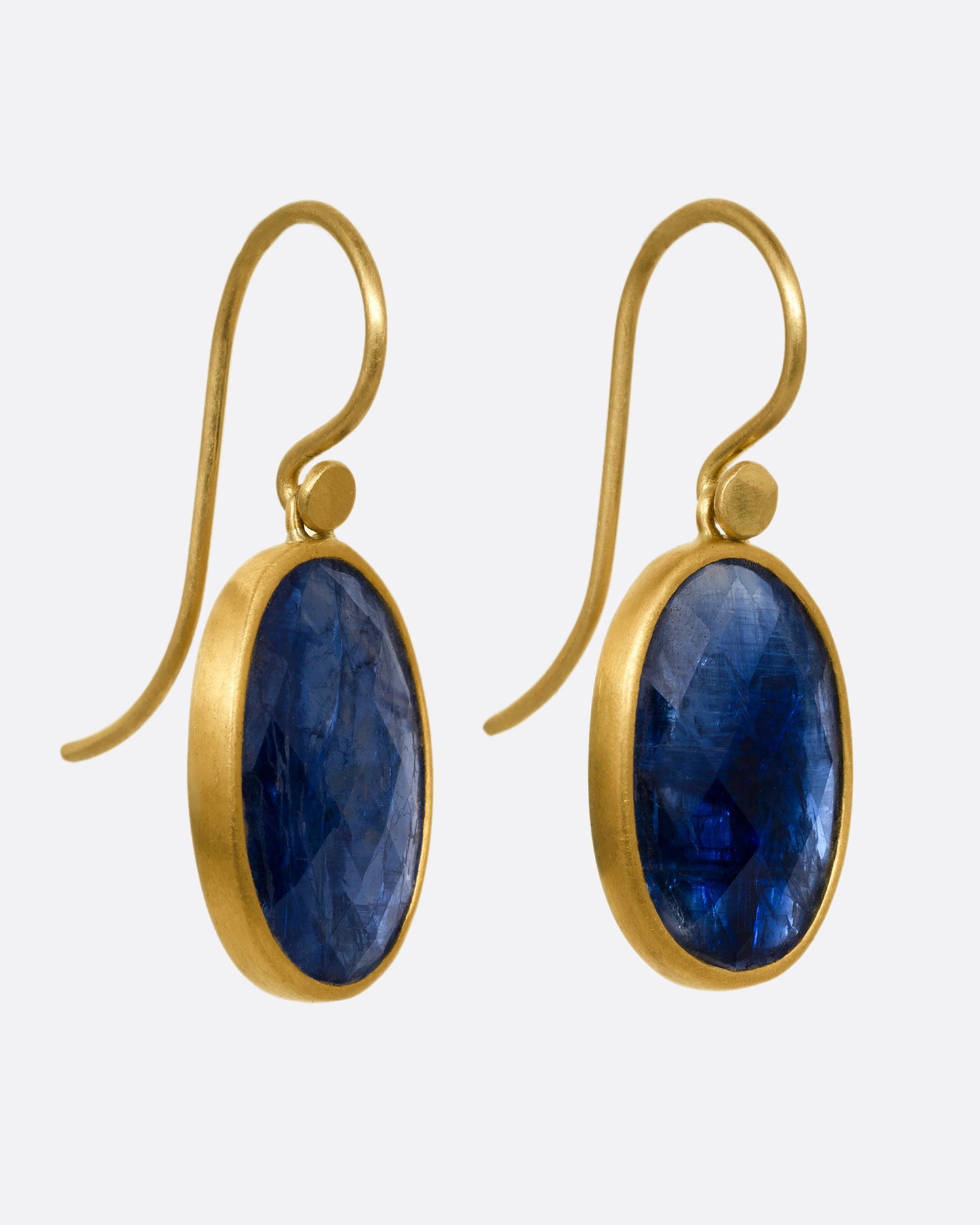 A pair of faceted blue kyanite earrings with yellow gold bezels and ear hooks. Shown from the side.