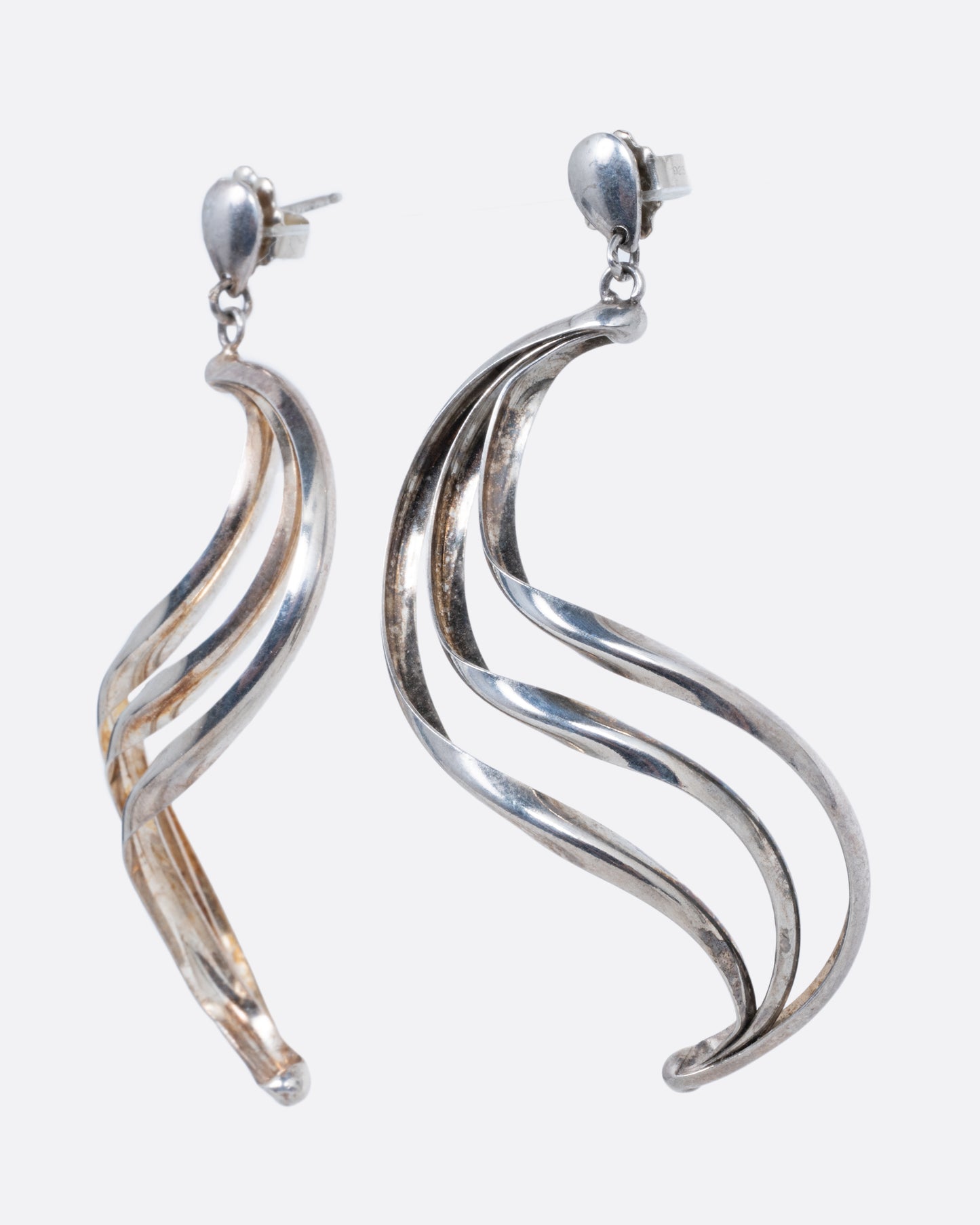 Silver dangle earrings with stud tops and three layers of silver ribbons in an S shape. Shown standing up from the side.