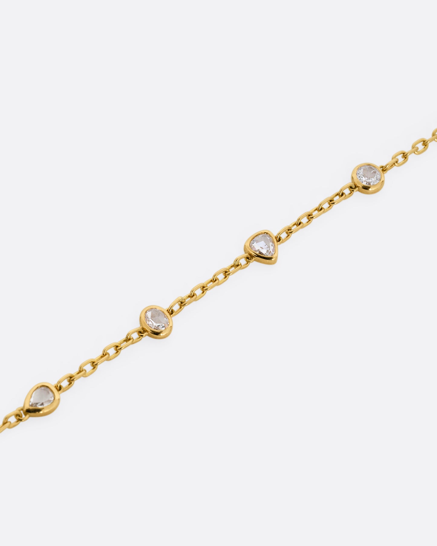 A yellow gold cable chain bracelet with four bezel set diamonds. Shown lying flat at an angle.