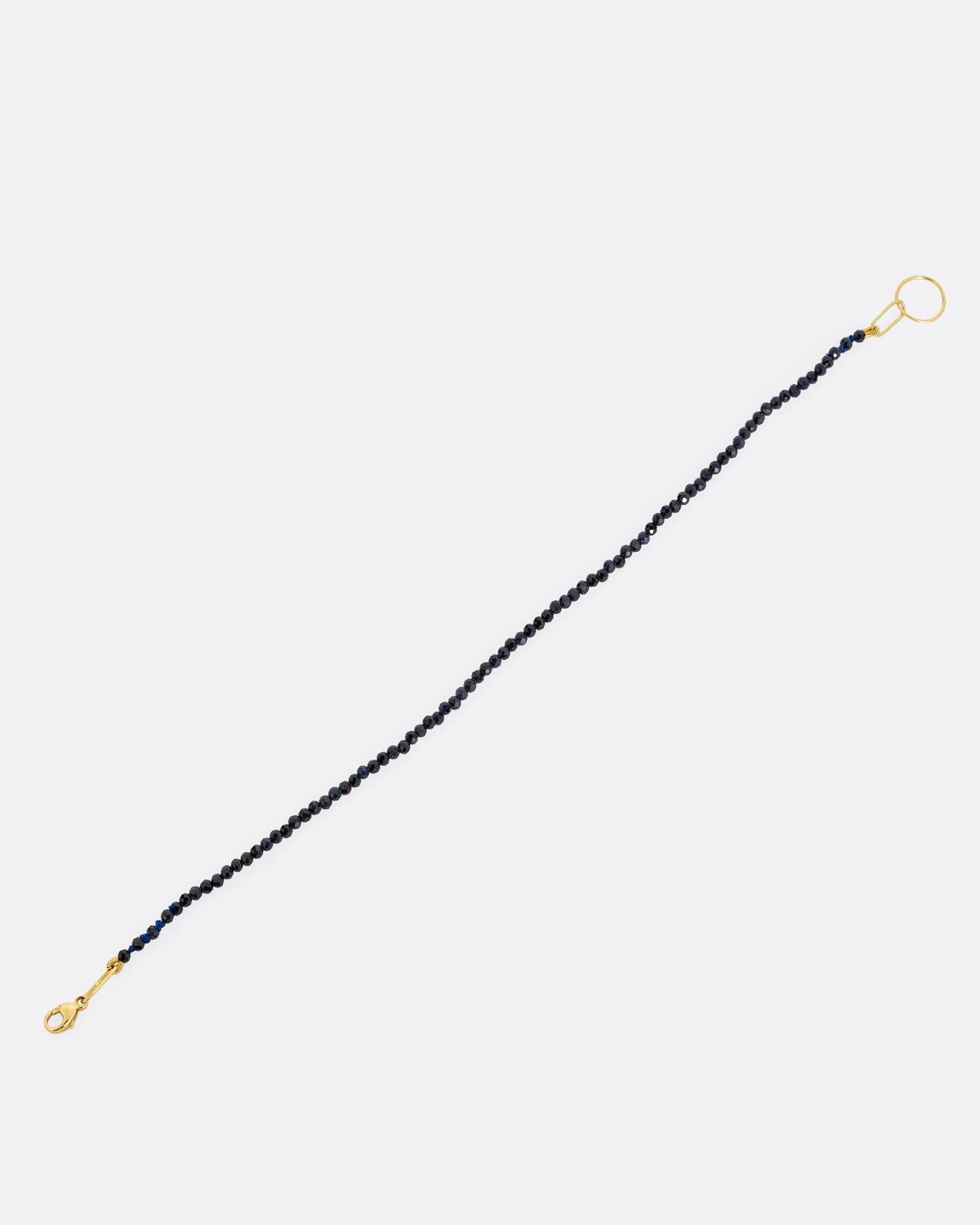 A beaded blue sapphire bracelet with a yellow gold clasp. Shown open from the side.