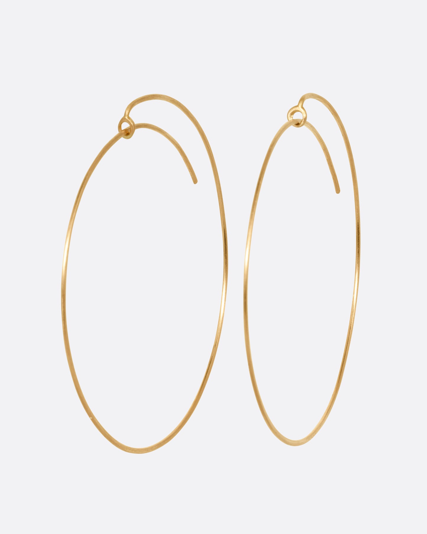 A pair of large yellow gold hoops with a minimalist wrap-around style top. Shown from the side.