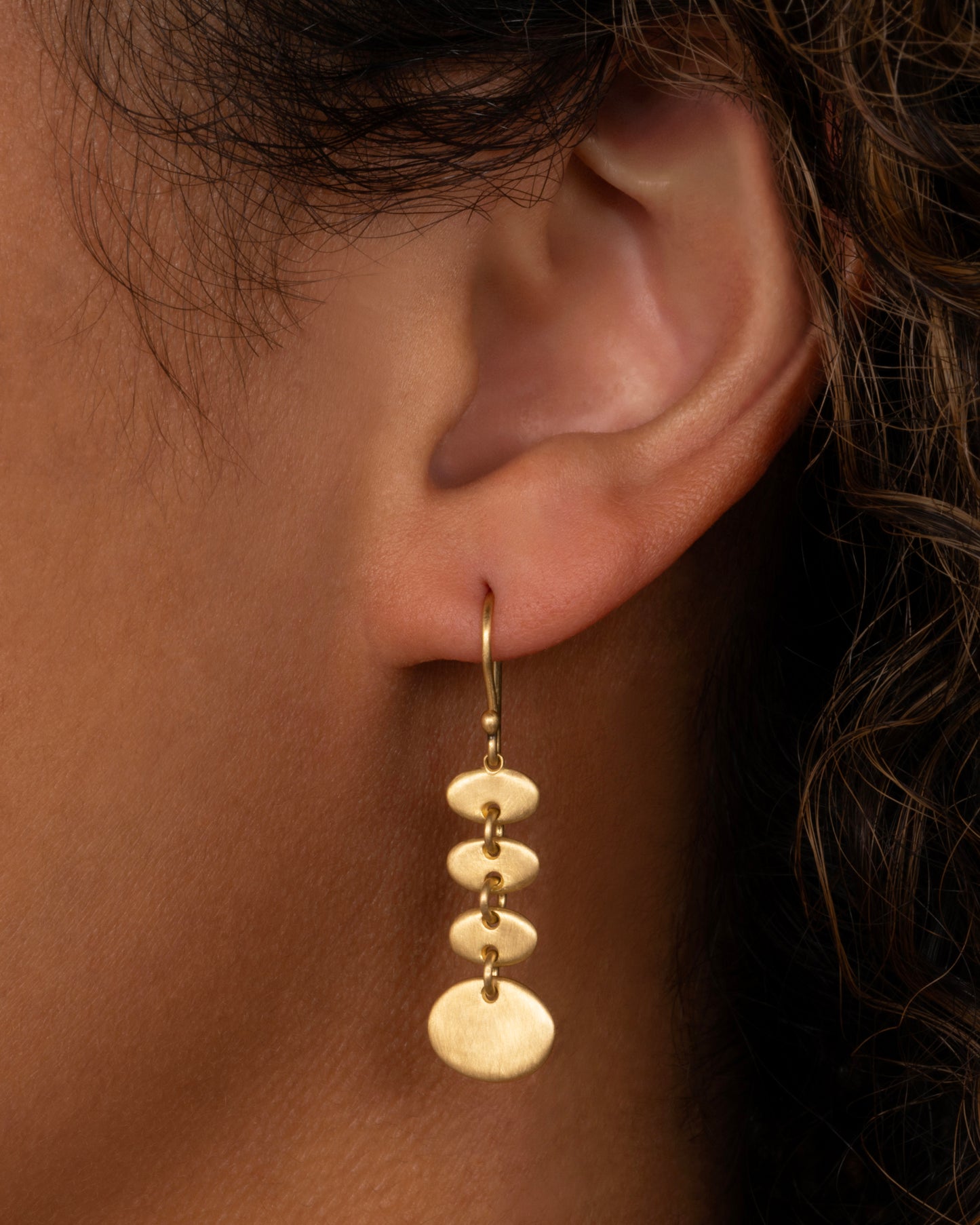 A yellow gold earring with linked graduated ovals. Shown from the front on a person.