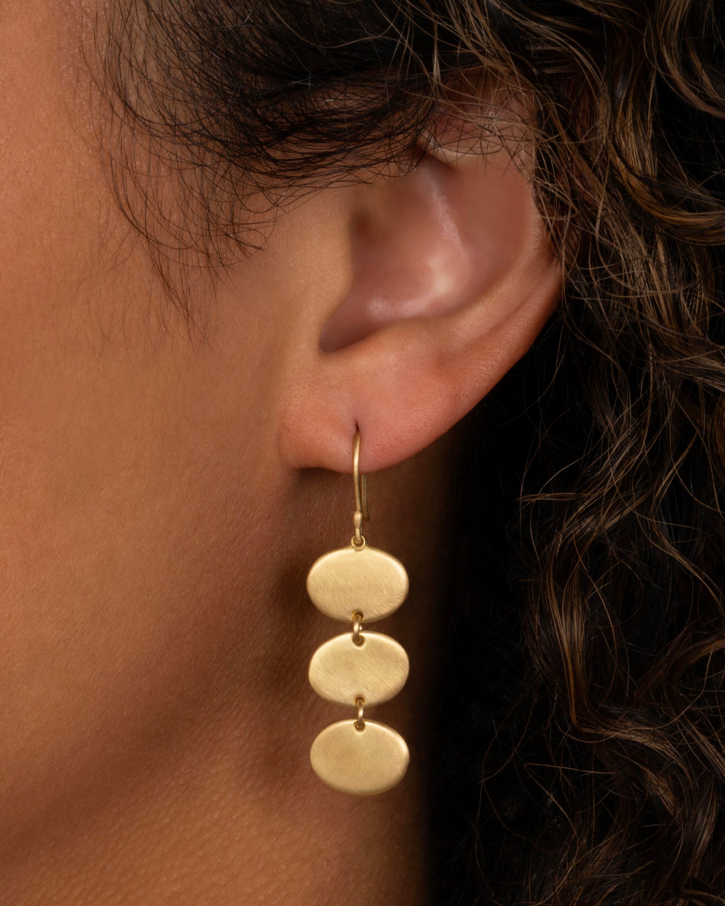 A yellow gold dangle earring with three linked ovals. Shown from the front on a person.