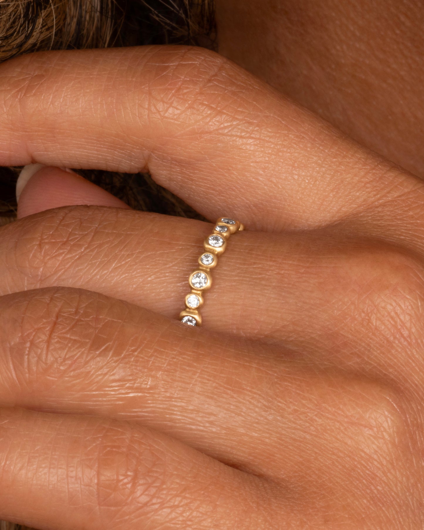 A yellow gold ring with a bubbly pattern of diamonds. Shown on a person from the side.
