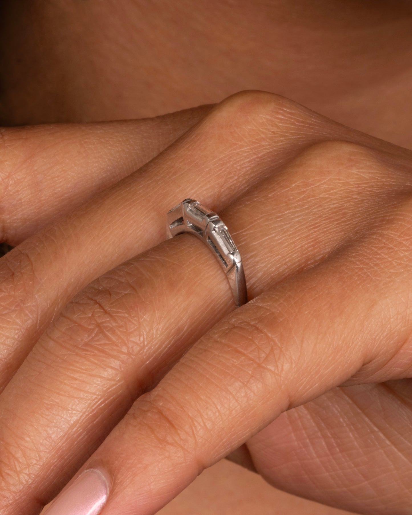 A platinum ring with three baguette diamonds. Shown worn on a finger.