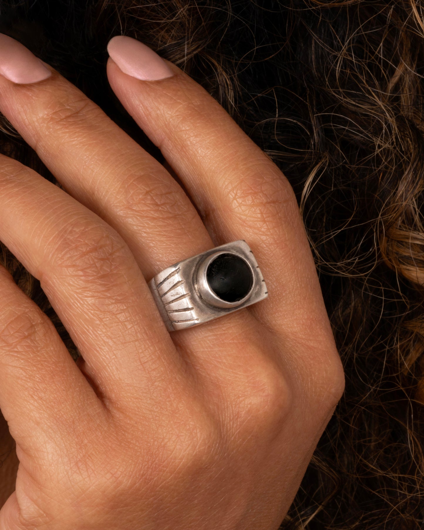 A silver ring with an oval onyx. Shown worn on a finger.