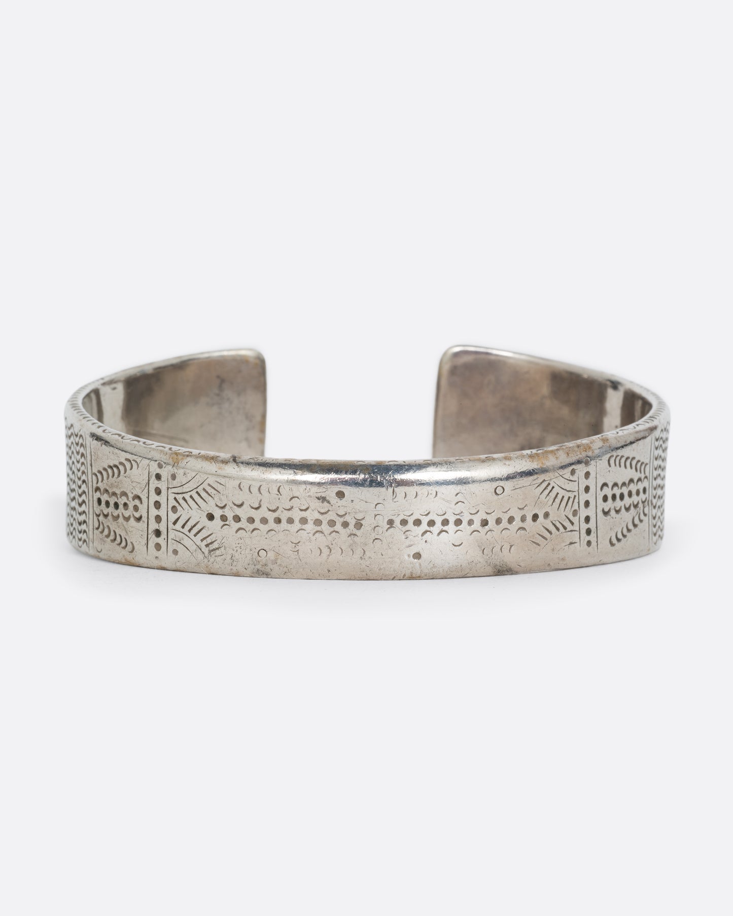 A silver bracelet with a graduated silhouette, hand stamped pattern, and opening in the front. Shown from the back.