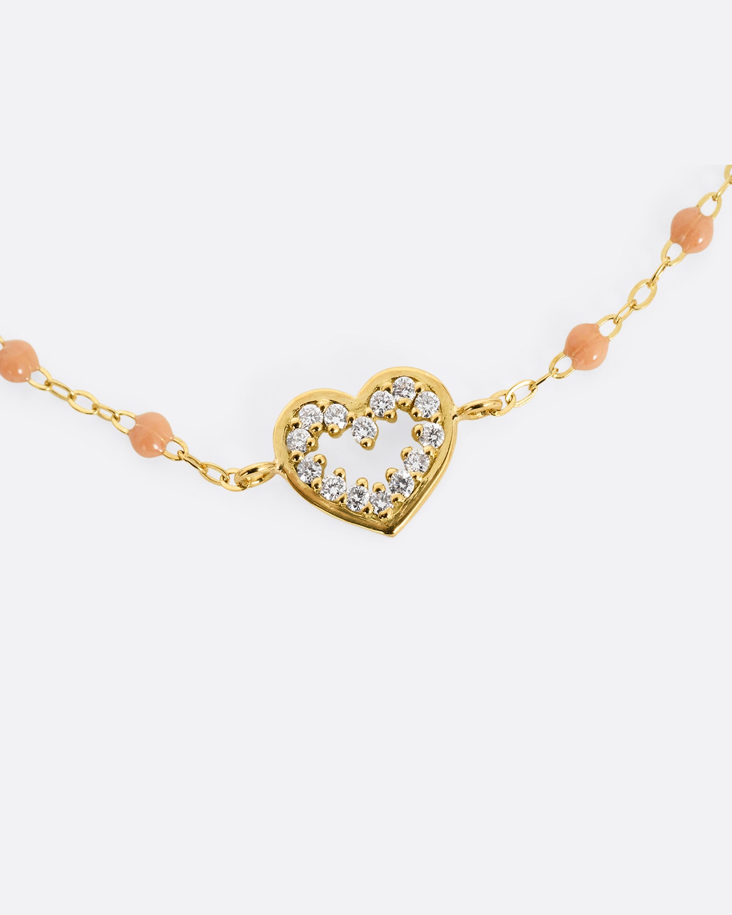 A close up of a yellow gold cable chain bracelet with a diamond lined heart charm and caramel brown resin droplets throughout.