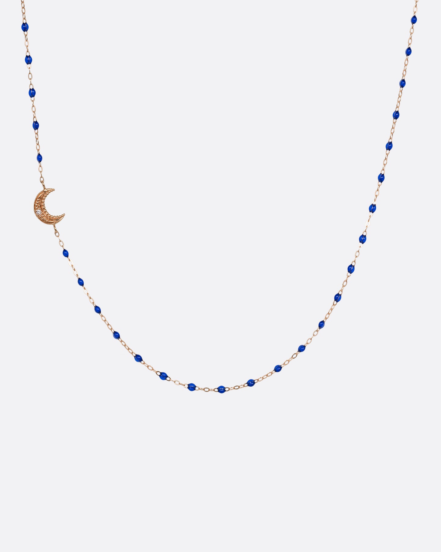 A rose gold cable chain necklace with lapis blue resin droplets along the chain and a crescent moon charm with a diamond on one side. Shown from the front.