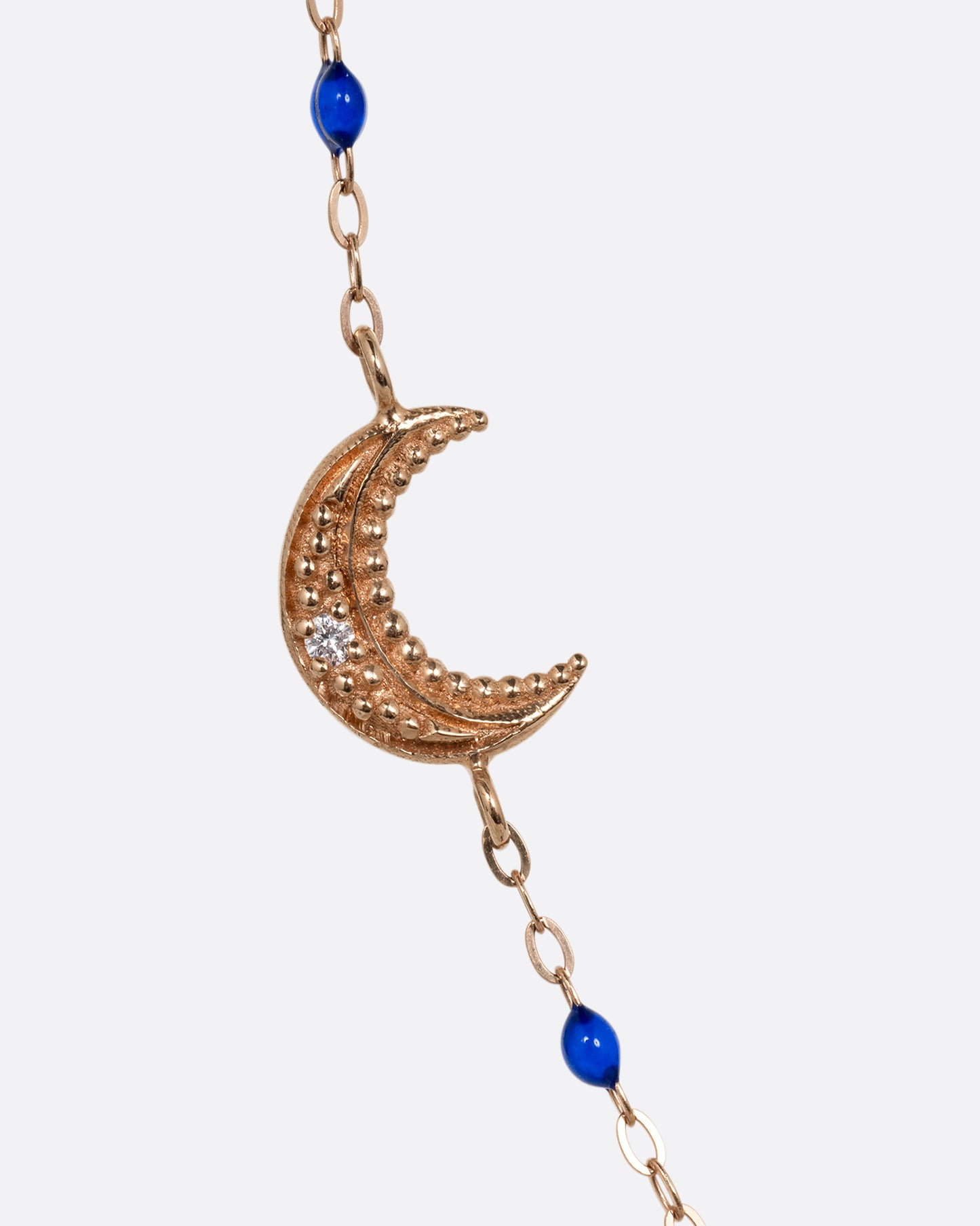 A close up of a rose gold cable chain necklace with lapis blue resin droplets along the chain and a crescent moon charm with a diamond. Shown from the front.