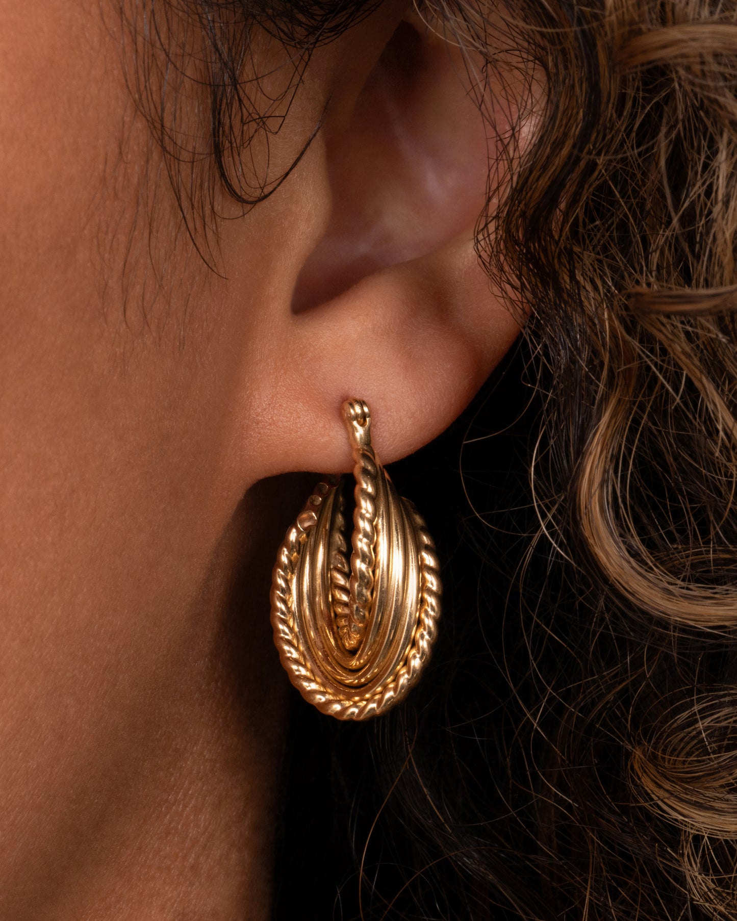 A yellow gold earring with layers of twisted loops and click tops. Shown from the front on a person.