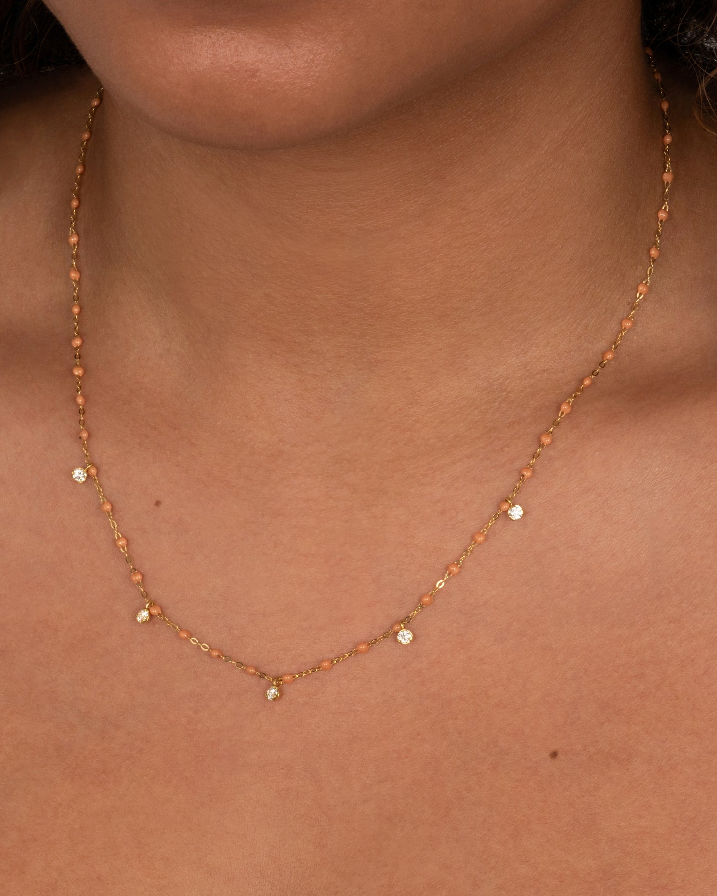 A yellow gold cable chain necklace with caramel brown resin droplets along the chain and five dangling diamond charms. Shown on a person from the front.