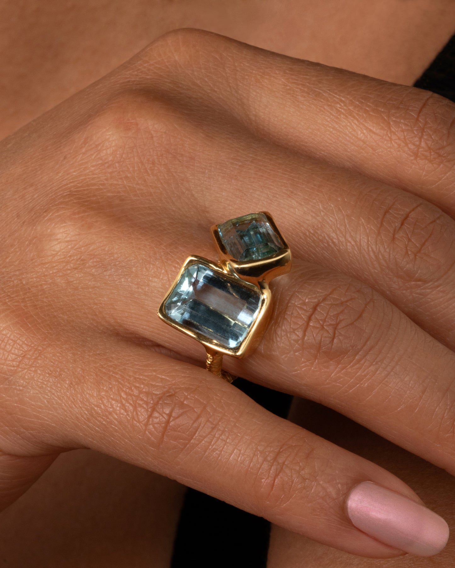 A yellow gold ring featuring two large emerald cut aquamarines set slightly askew. shown on a finger