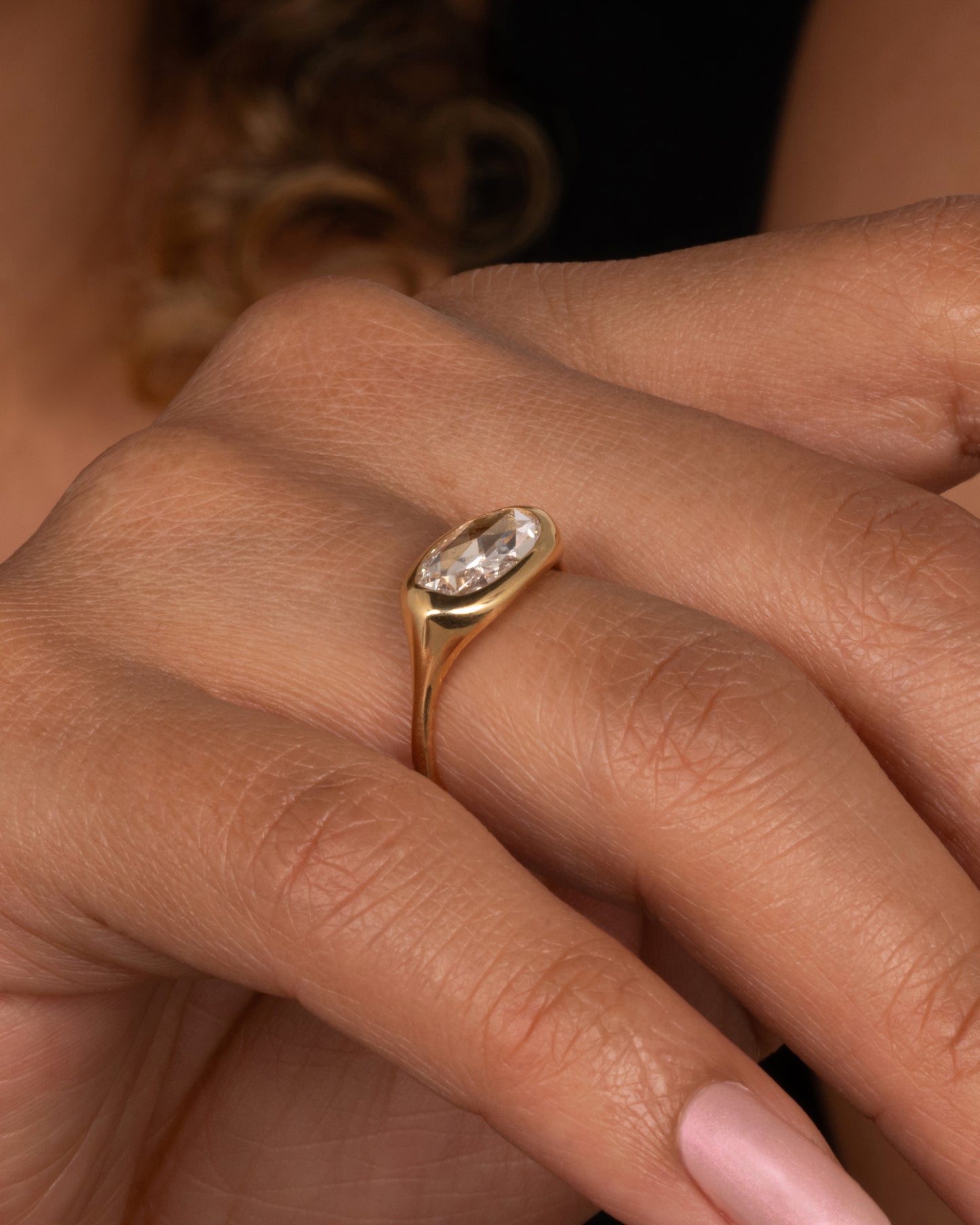 A yellow gold ring with a n oval rose cut diamond. Shown on a finger.