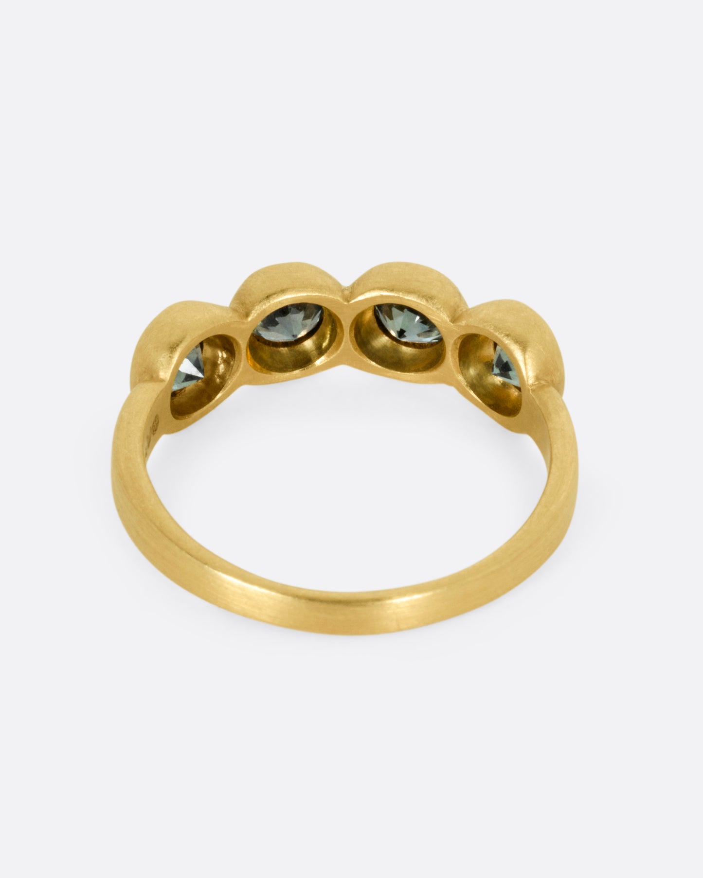 A yellow gold ring with four bezel set green sapphires, shown from the back.