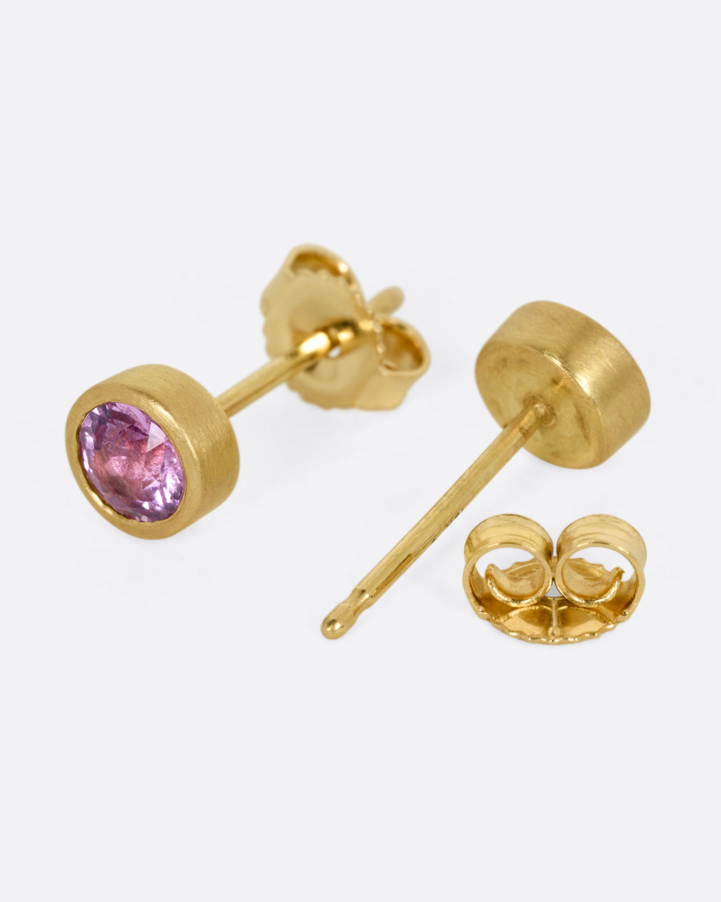 A pair of yellow gold stud earrings with pink sapphires. One earring is shown from the front, the other is open from the back.