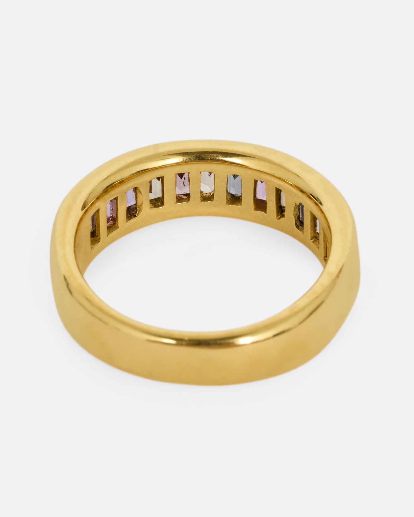 A yellow gold ring with channel set multicolored sapphires. Shown from the back.
