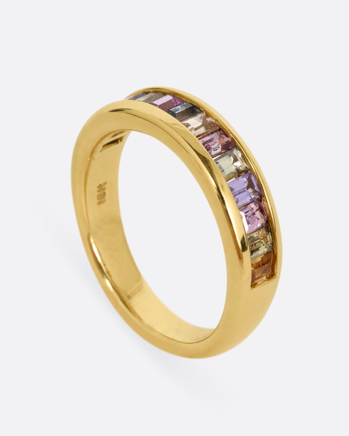 A yellow gold ring with channel set multicolored sapphires. Shown standing up from the side.
