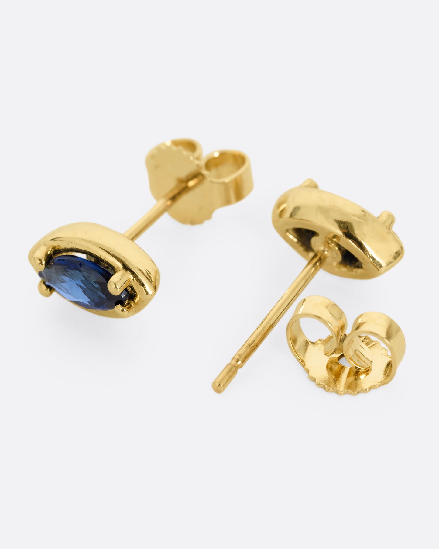 A pair of yellow gold eye shaped earrings with marquise blue sapphires. Shown lying flat; one from the front, the other open from the back.