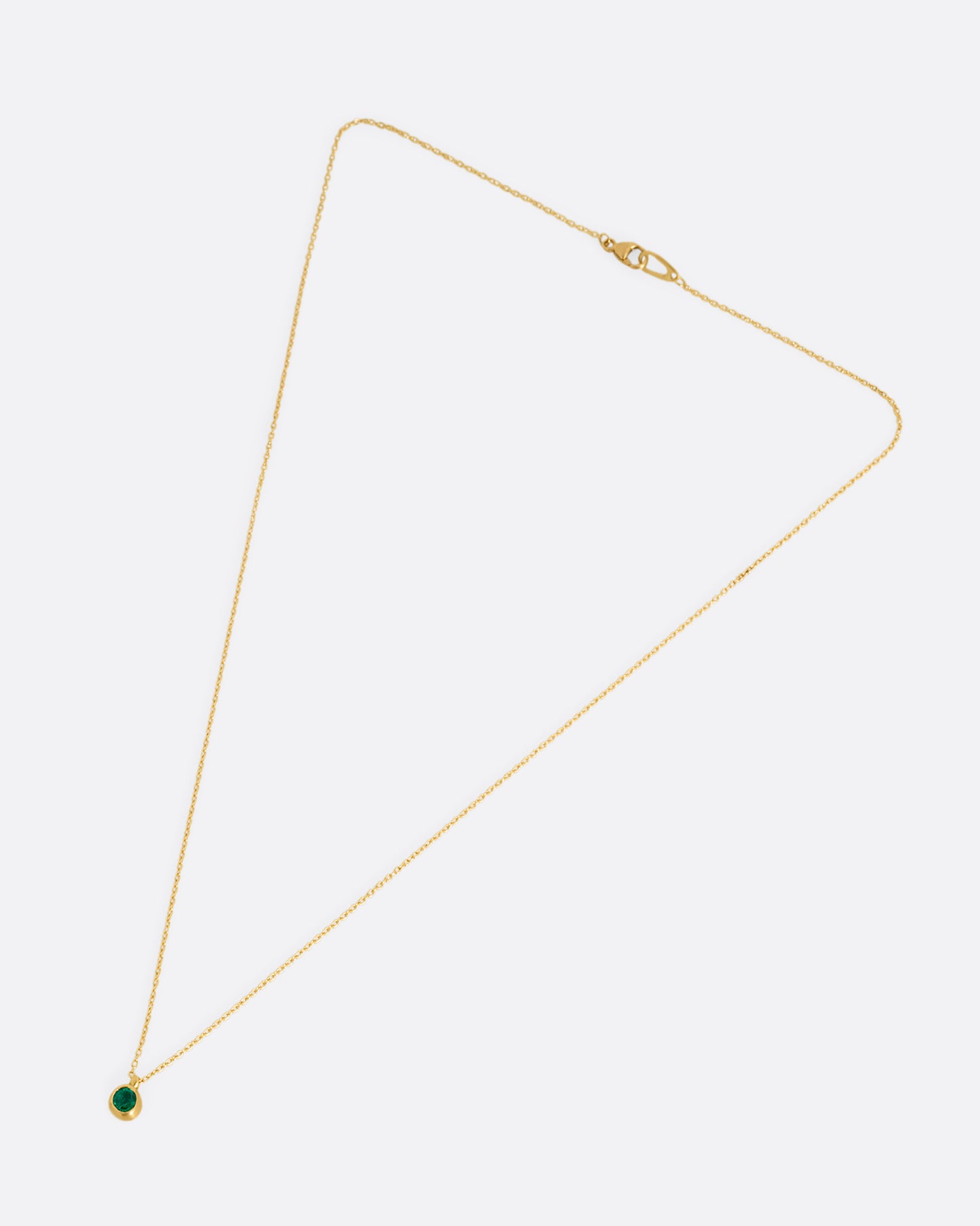 A yellow gold cable chain necklace with a faceted emerald in a satiny gold bezel. Shown clasped lying flat from the front.