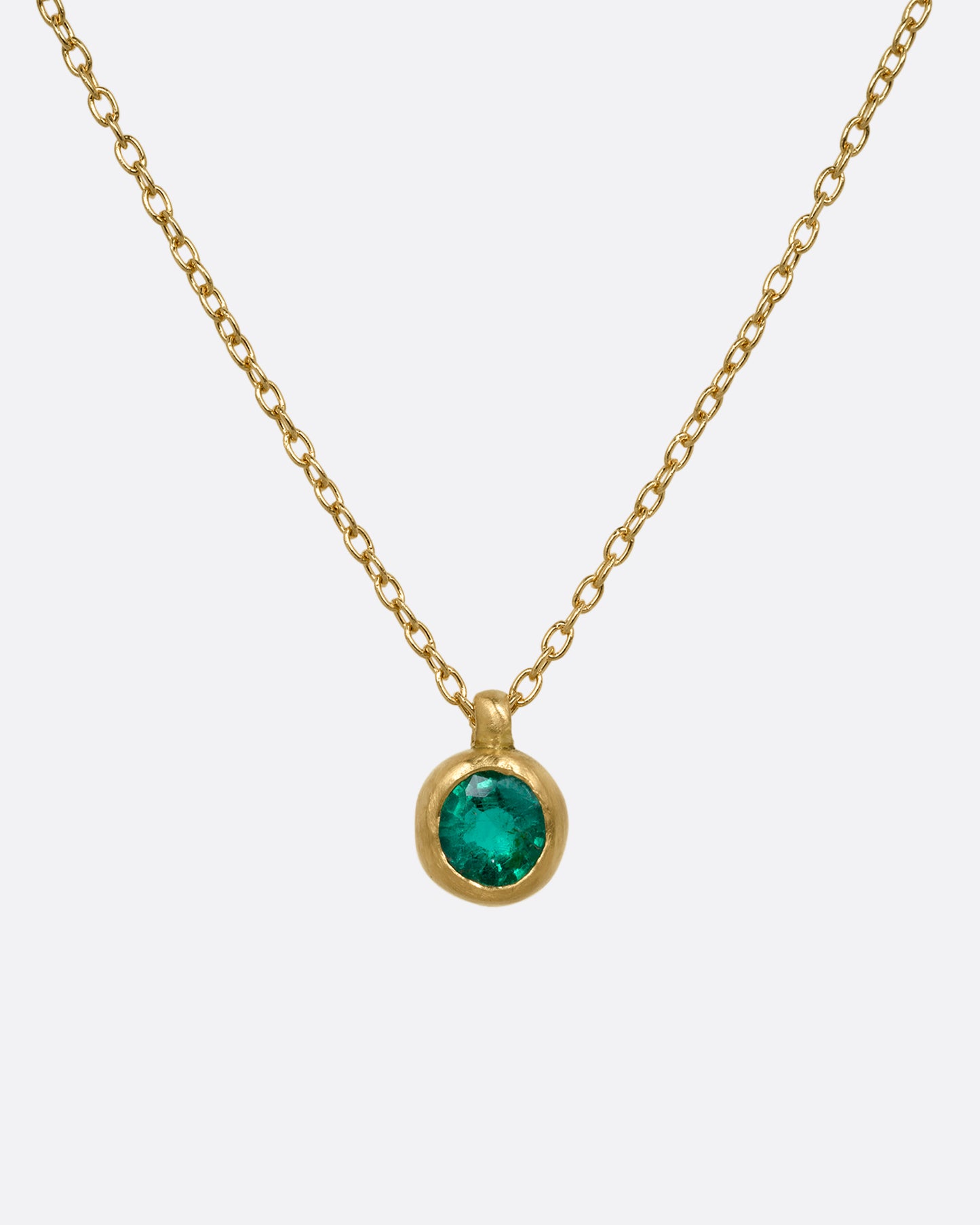A yellow gold cable chain necklace with a faceted emerald in a satiny gold bezel. Shown from the front.