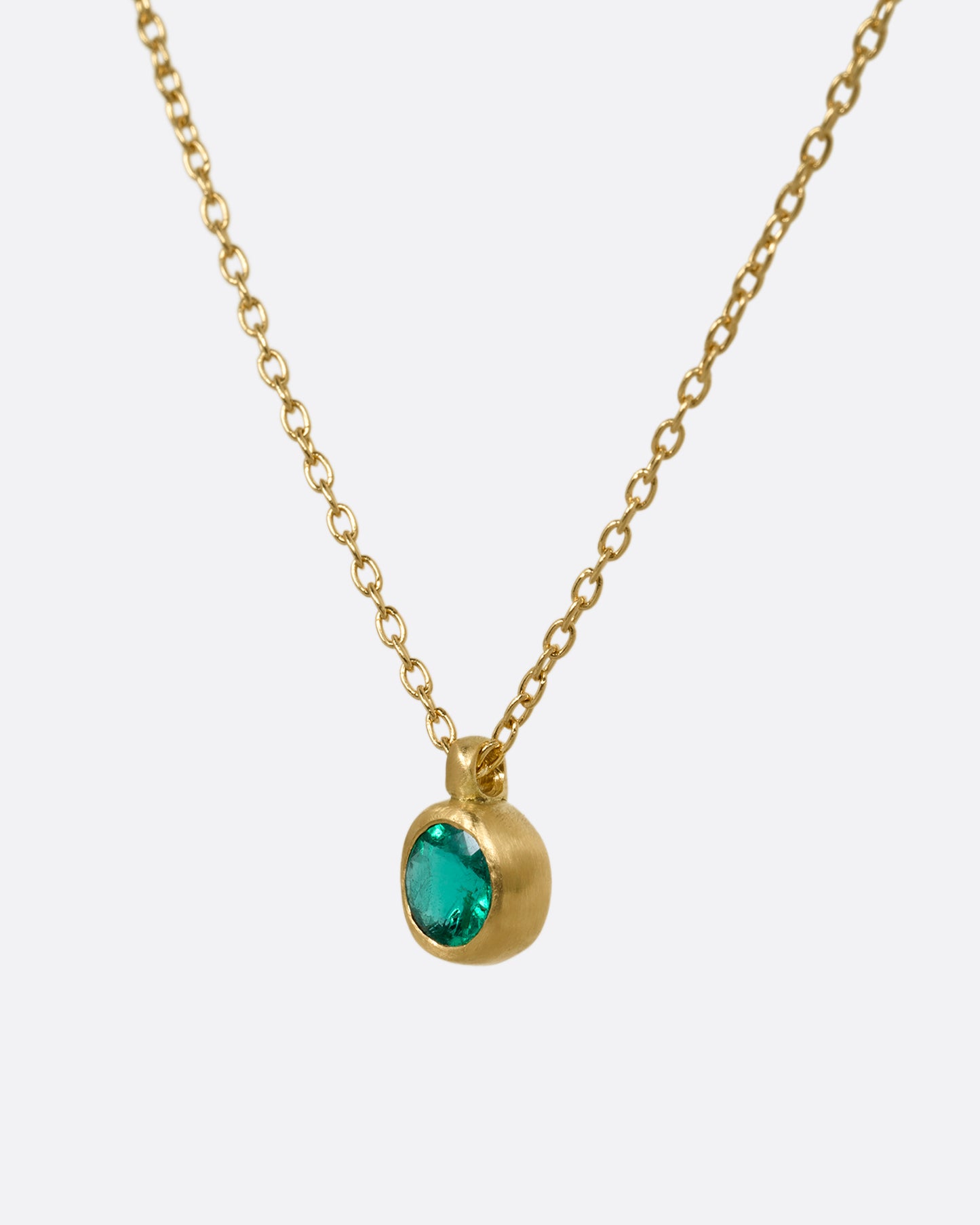 A yellow gold cable chain necklace with a faceted emerald in a satiny gold bezel. Shown from the side.