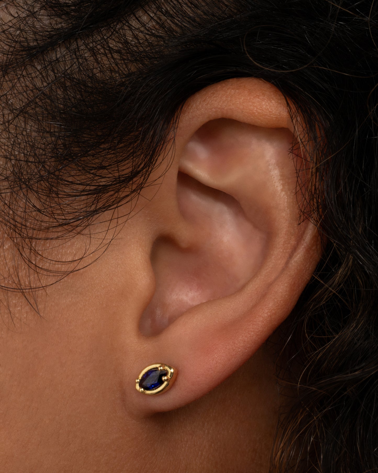 A yellow gold eye shaped earring with a marquise blue sapphire. Shown from the front on a person.