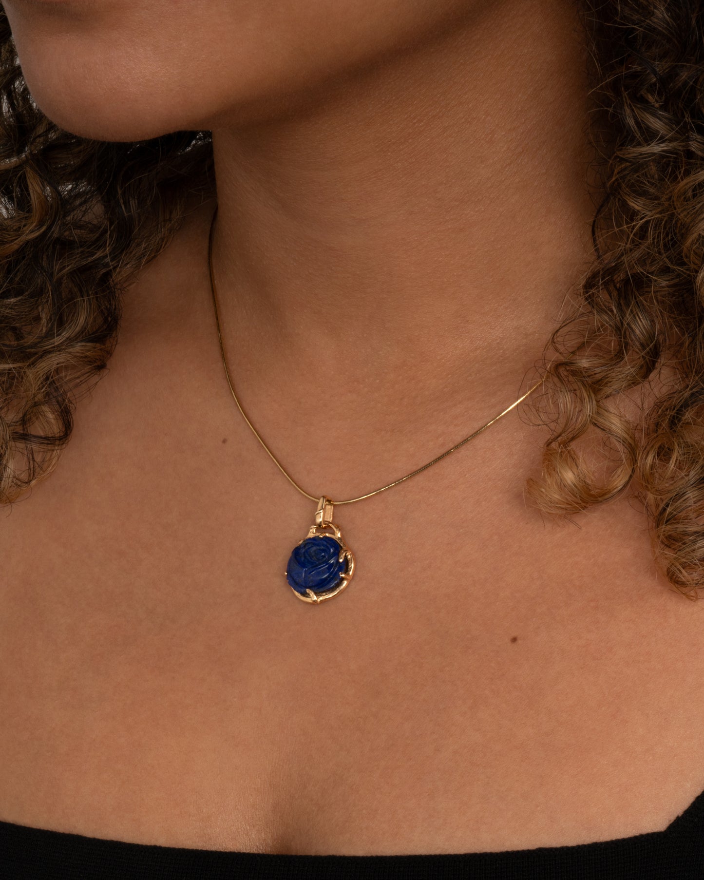 yellow gold rose shaped lapis charm shown worn on a snake chain around the neck