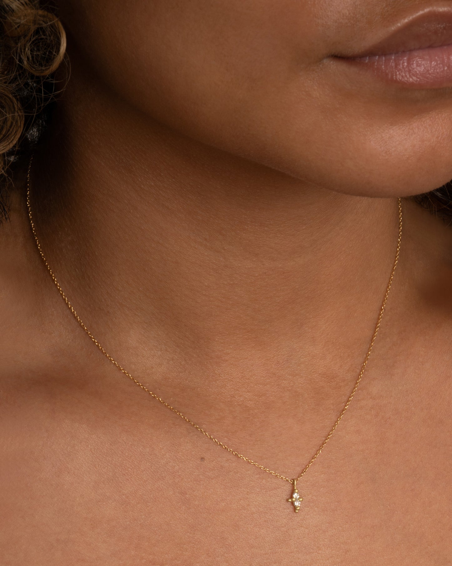 A yellow gold necklace with a double white diamond pendant. Shown worn around a neck.