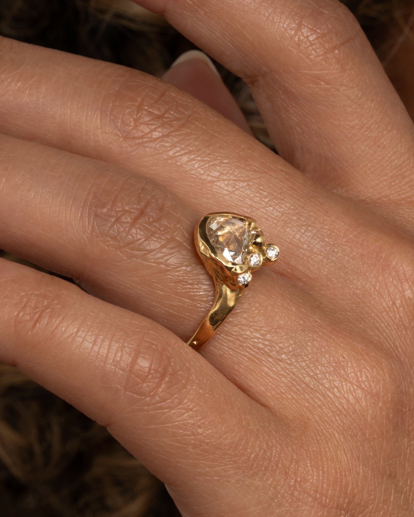 A yellow gold ring with a central rose cut diamond half moon and bezel set diamond accents on top of the flat side. Shown from the side on a hand with the flat side facing down.